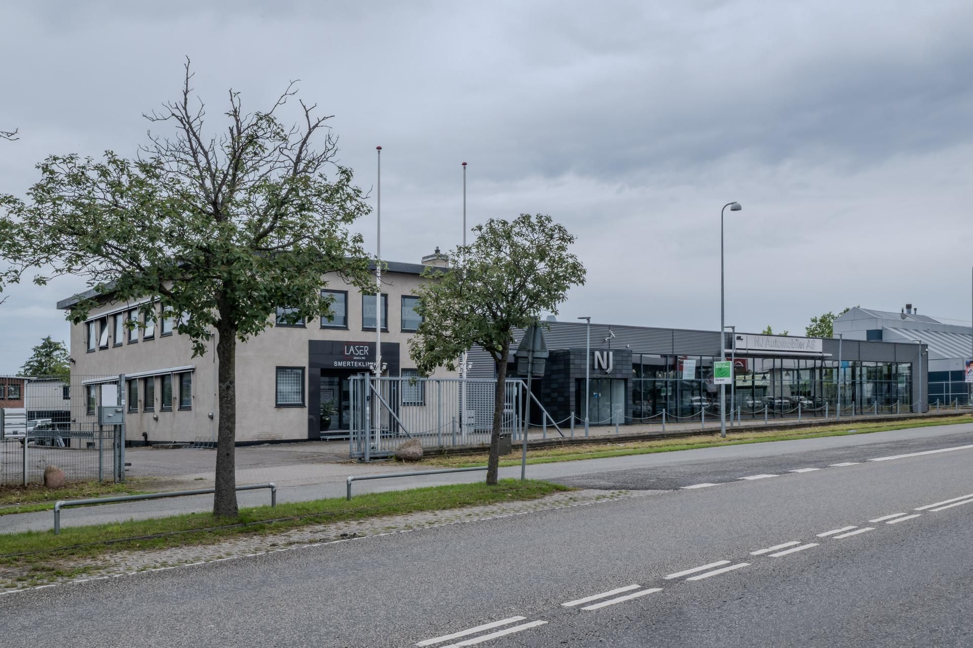 Vej langs moderne forretningsbygninger med glasvinduer og skrifttyper som Laser og NJ