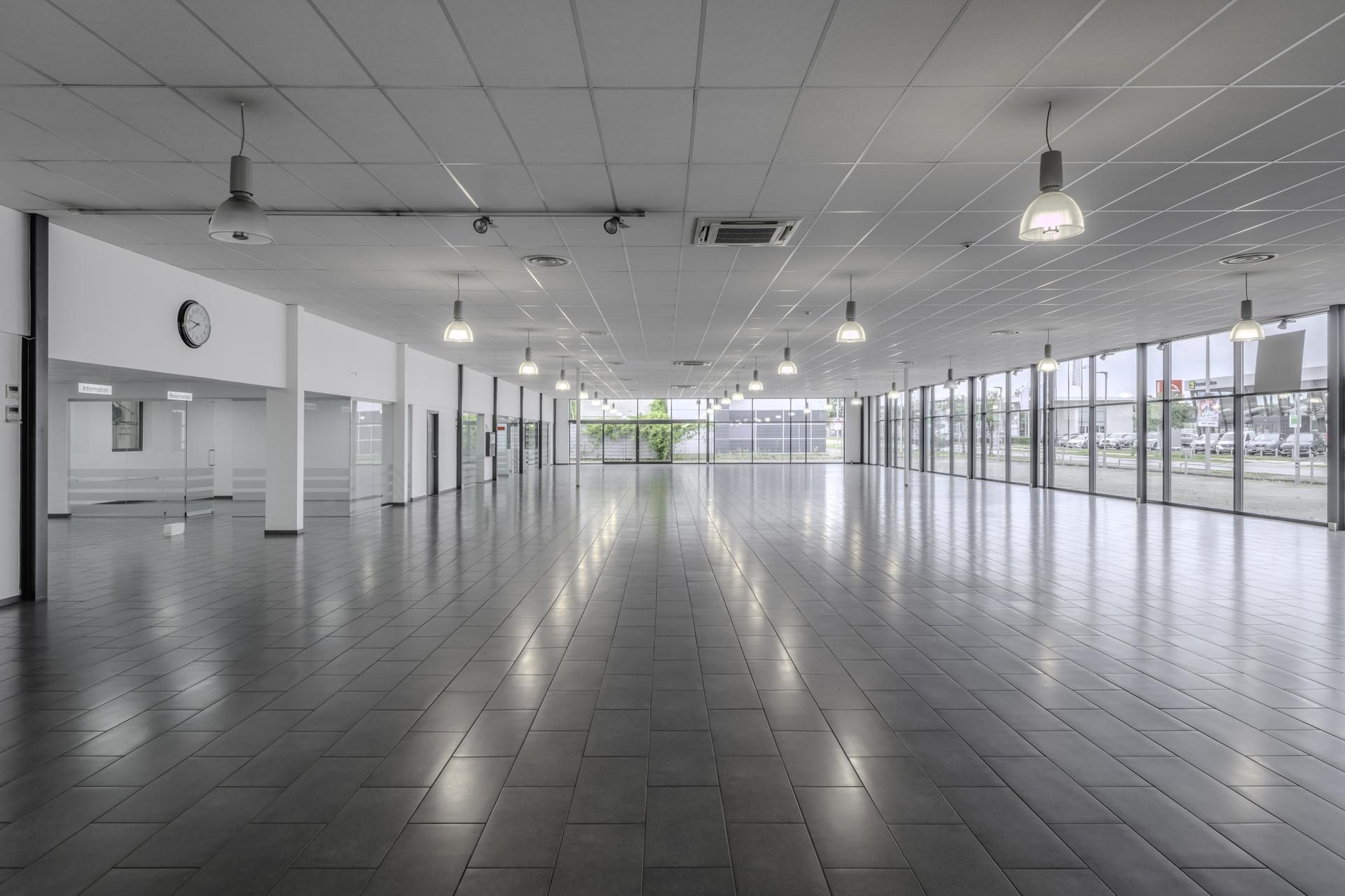 Moderne lobby med hvid loft, glasvinduer, store sortfliserede gulve, hængelampe og klokke på væggen