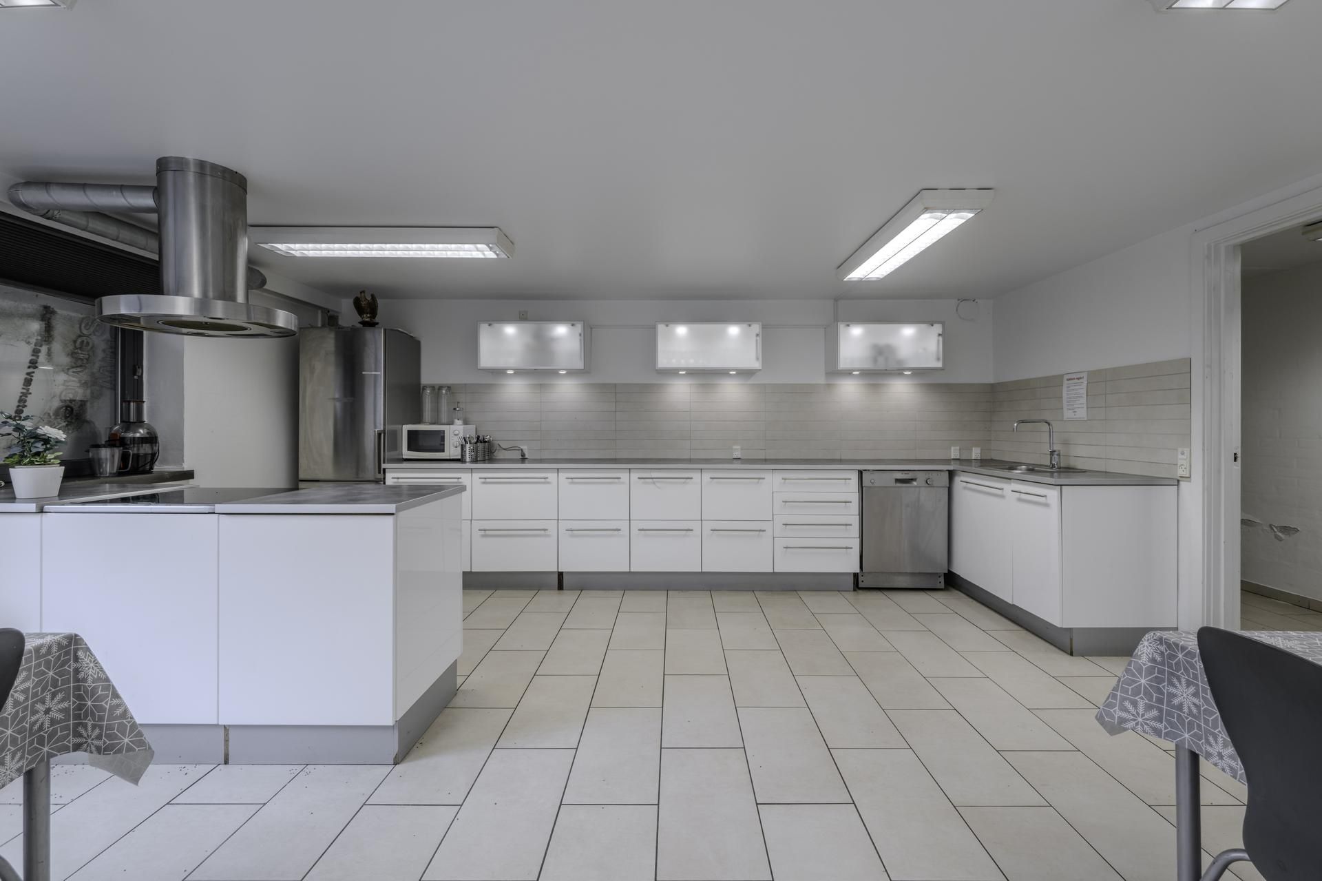 Moderne køkken med hvide køkkenskabe og apparater, en stor ø og en stor vinduesglas. Lyse gulvfliser og en åben dør til siden