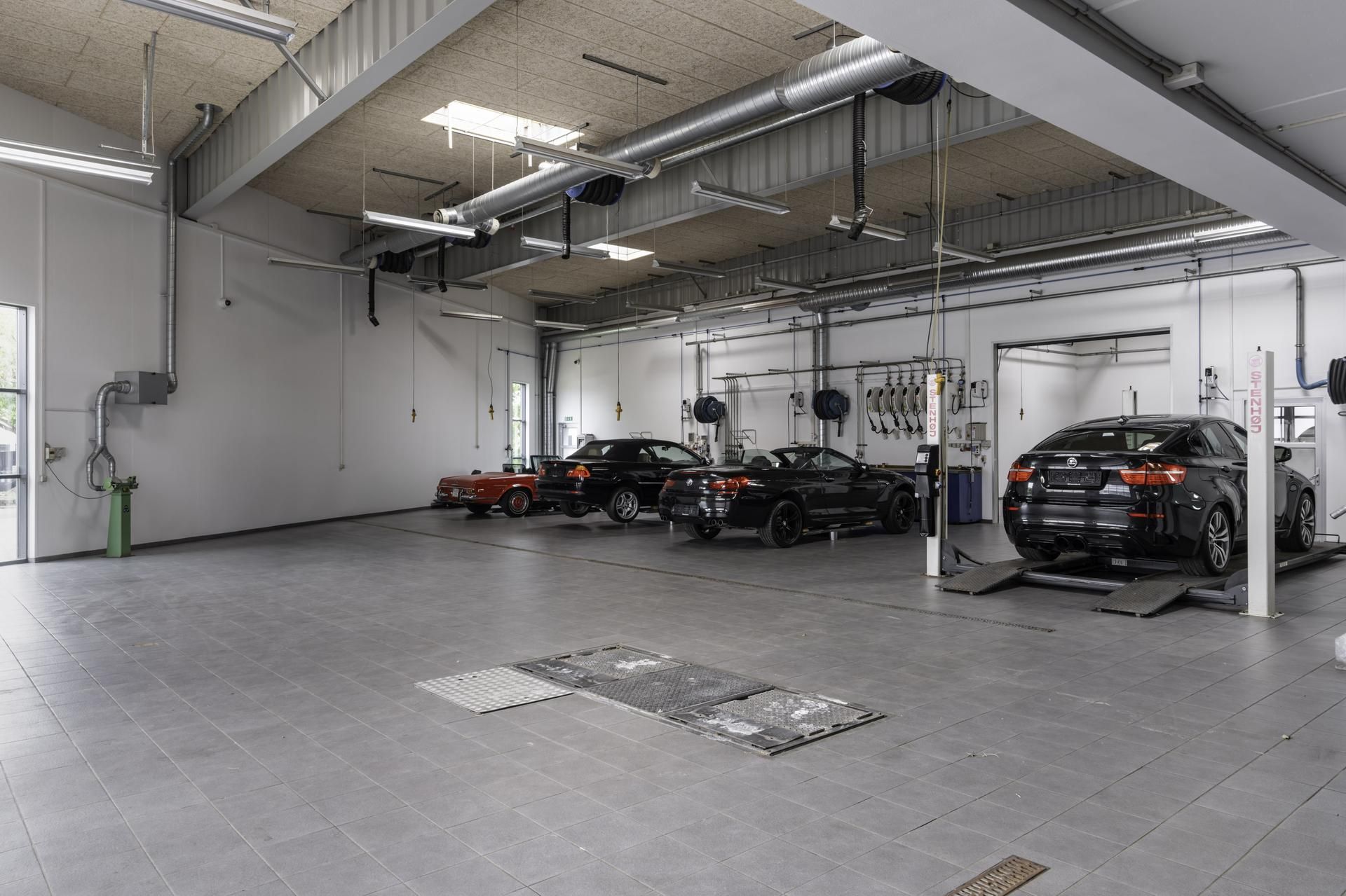 Garage med flere biler på højloftede lift, forskellige biler, forskellige værktøjer og maskiner samt lysegule loftsbælte