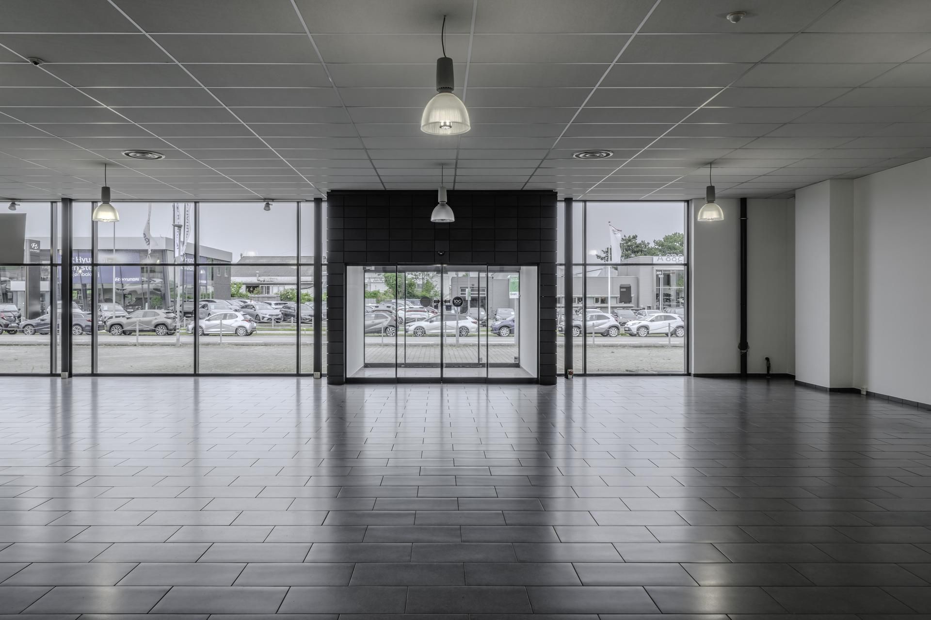 Moderne showroom med stort glasvinduesparti og åbne døre til udstillingsområdet med biler i baggrunden