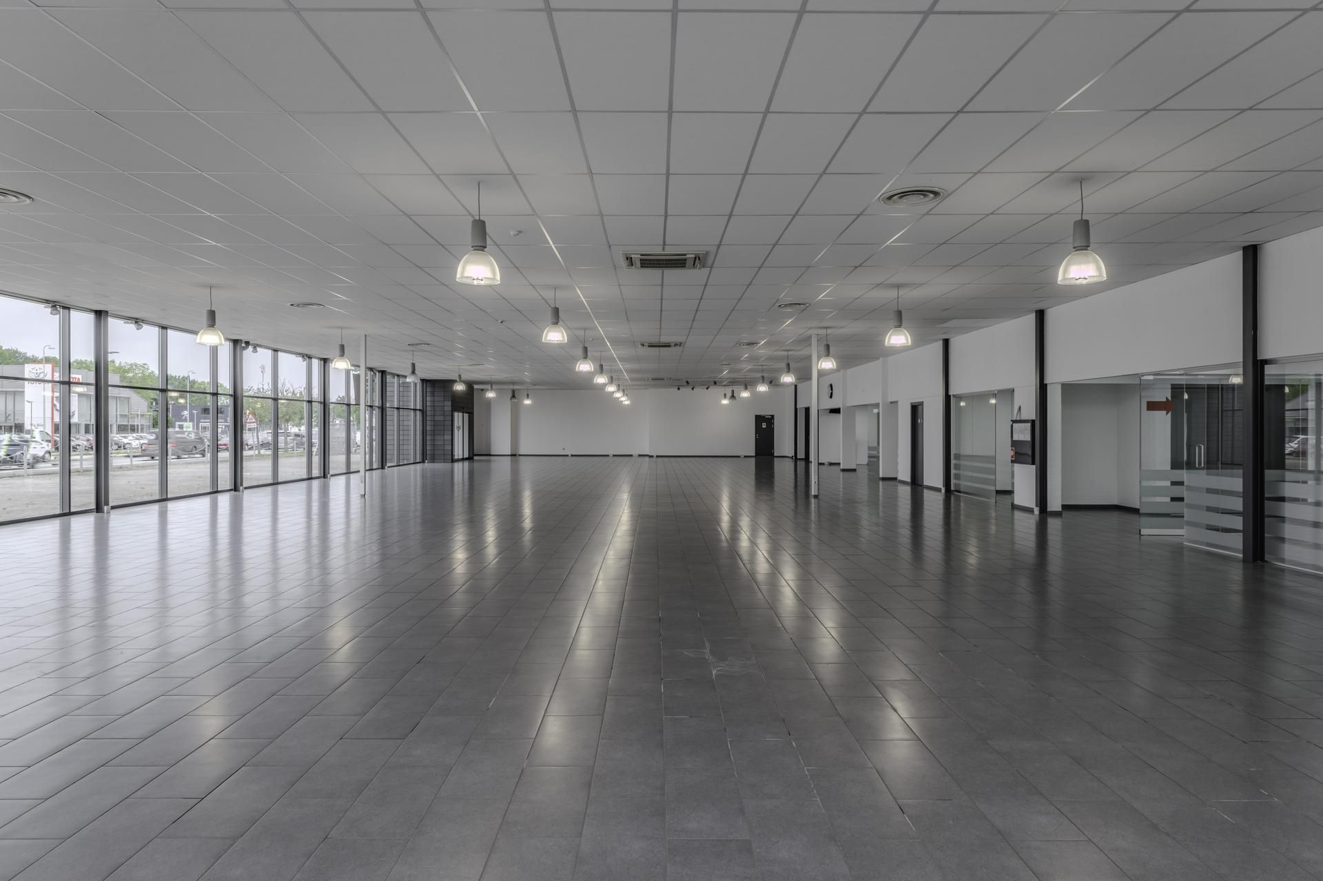 Langt, tomt lokale med store vinduer og hvide lofter og vægge. Lamper er installeret i loftet, og de reflekterer stærkt på