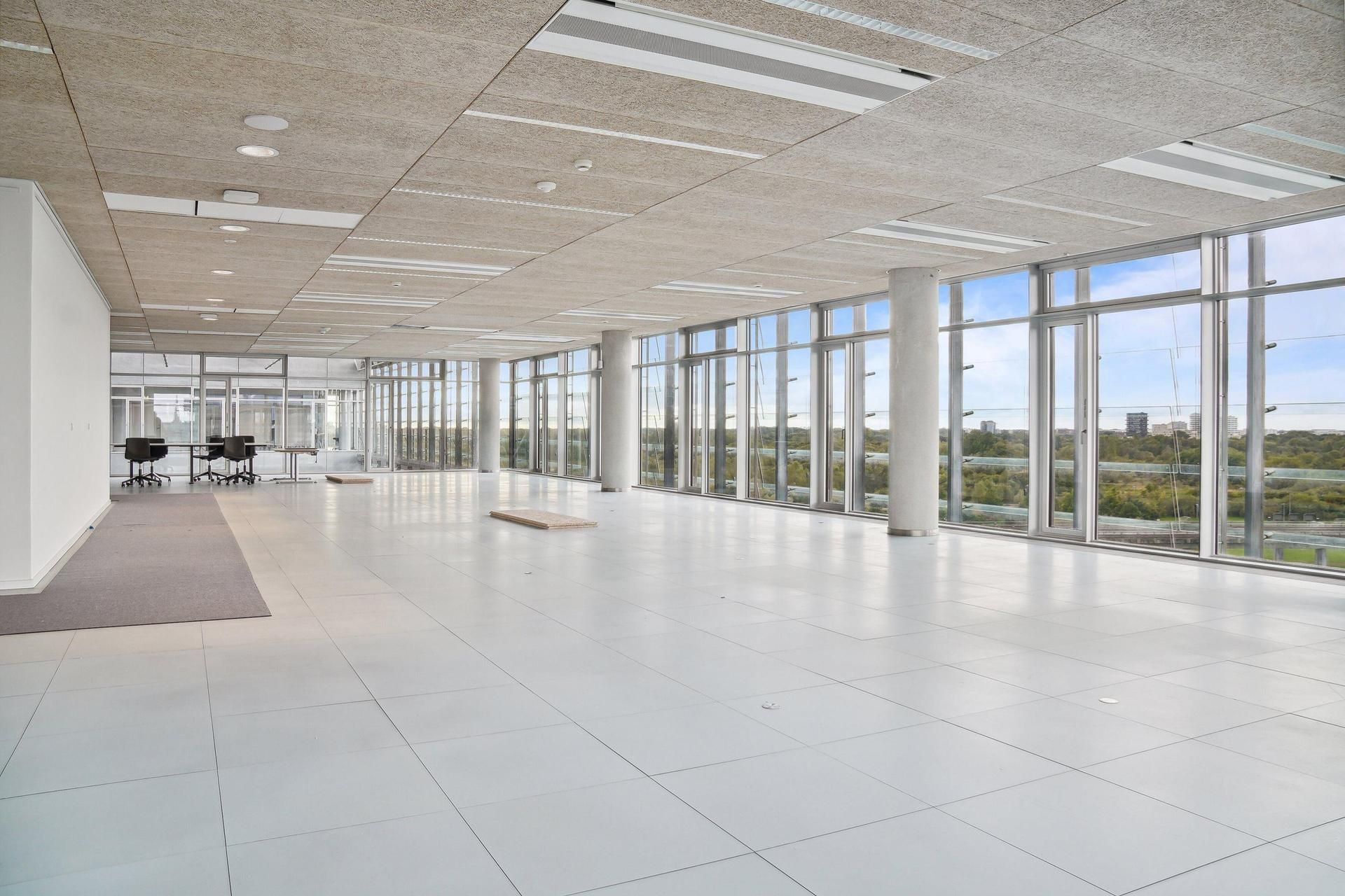 Store glasvinduer med udsigt over Amager Fælled og byen i baggrunden, hvide paneler, hvide gulvfliser, højt loft og slanke