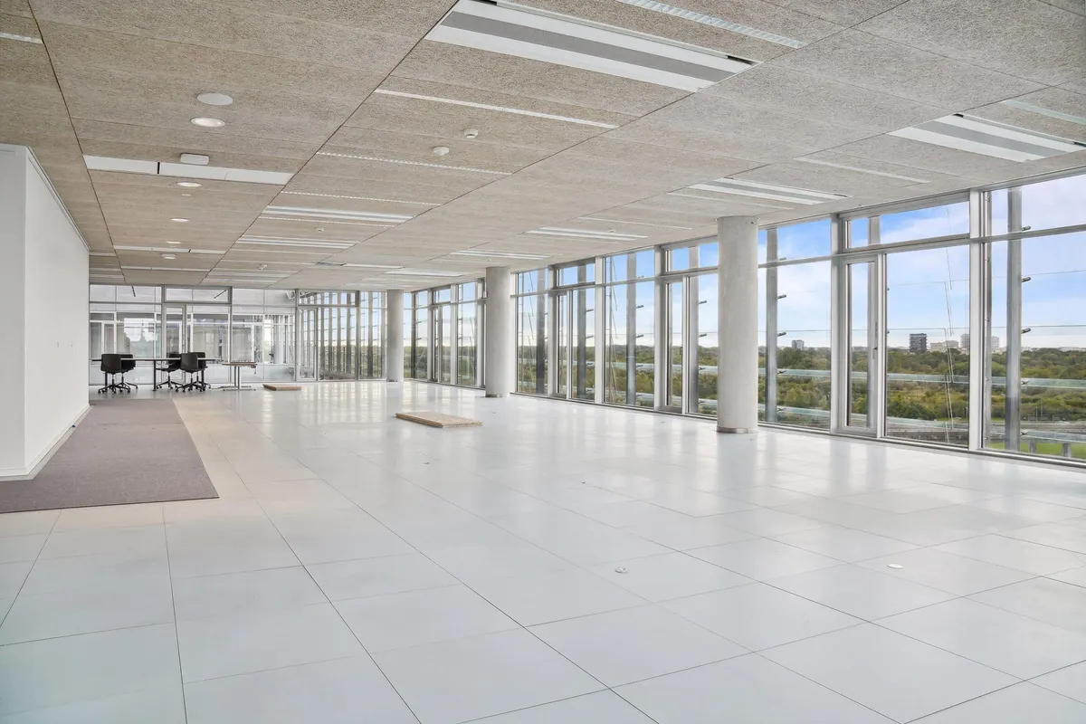 Store glasvinduer med udsigt over Amager Fælled og byen i baggrunden, hvide paneler, hvide gulvfliser, højt loft og slanke