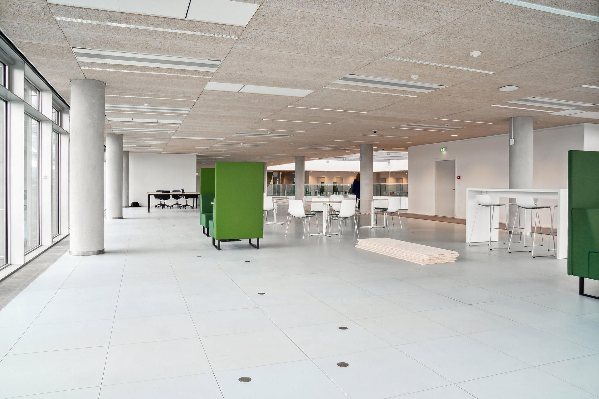 Indvendig i DR-byen ses et stort rum med hvide gulve, grønne kabiner og hvide stole samt flere høje, hvide søjler