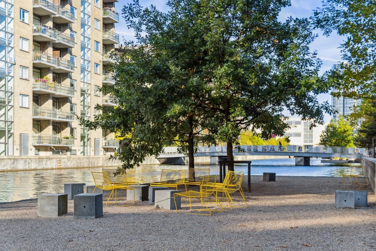Amager Fælledpark med moderne møbler og store bygninger i baggrunden, udsigt over vandet og en bro