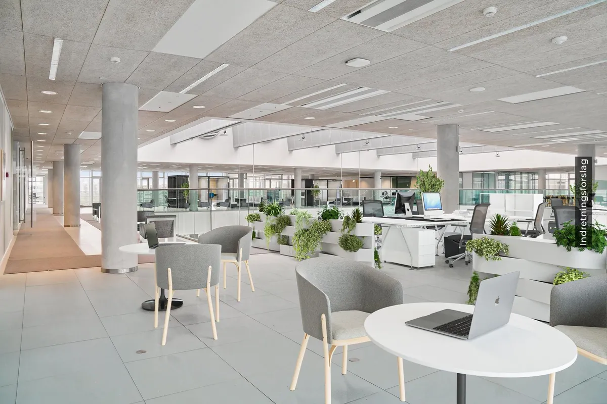 Moderne kontor med lyse lofter og møbler, hvor flere arbejdsborde og stole er placeret. En Apple-bærbar computer er åben på