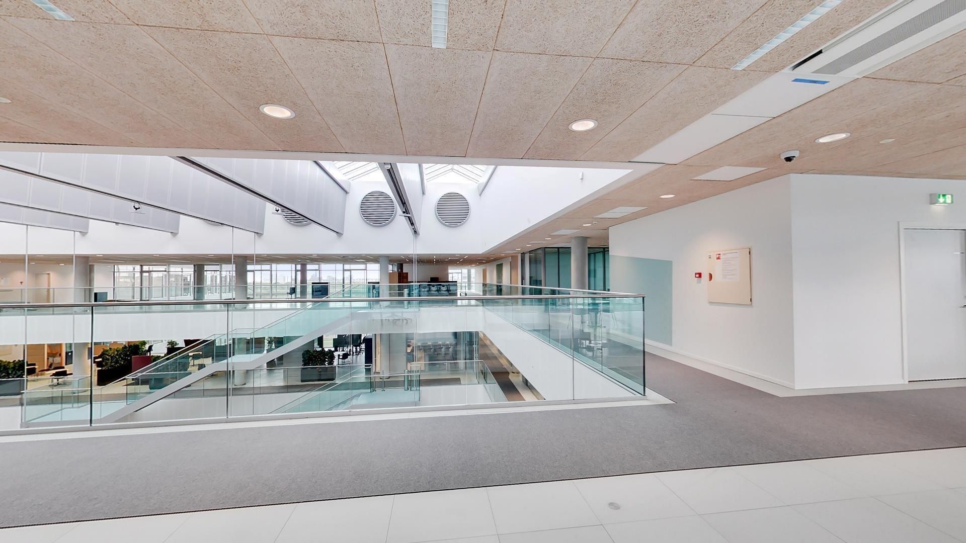 Moderne lobby med højt glasloft, hvid væg, gulv og loft samt stålbalustrade og røgdetektor på loftet