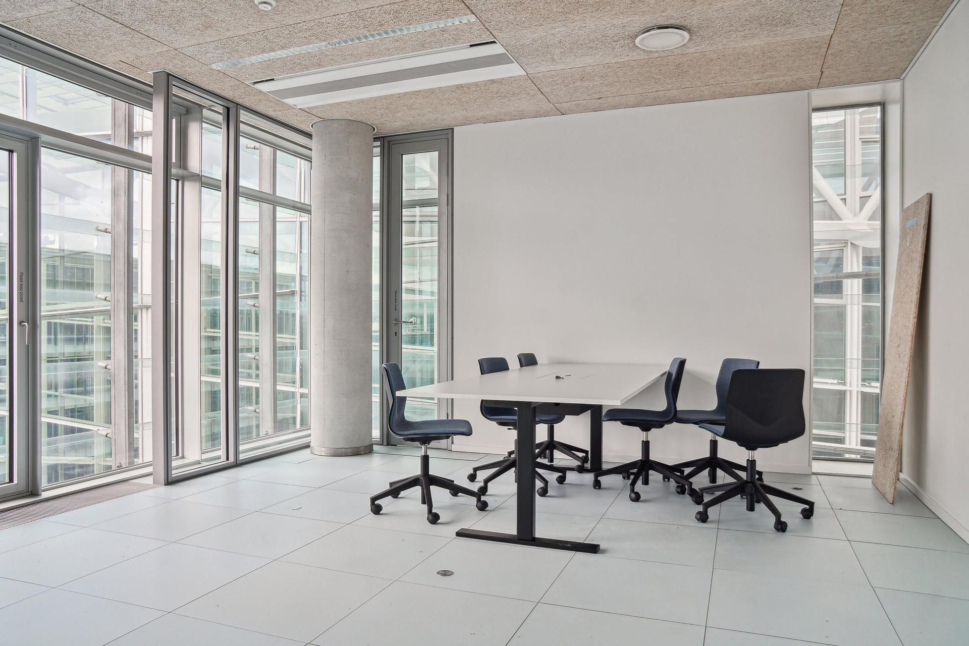 Moderne kontor med høje glasruder og et rektangulært bord med fem stole, alle i en minimalistisk stil, hvilket giver et