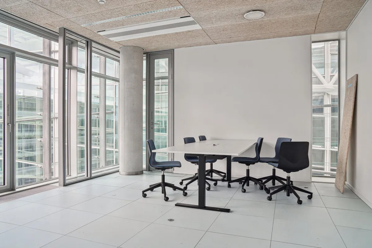 Moderne kontor med høje glasruder og et rektangulært bord med fem stole, alle i en minimalistisk stil, hvilket giver et