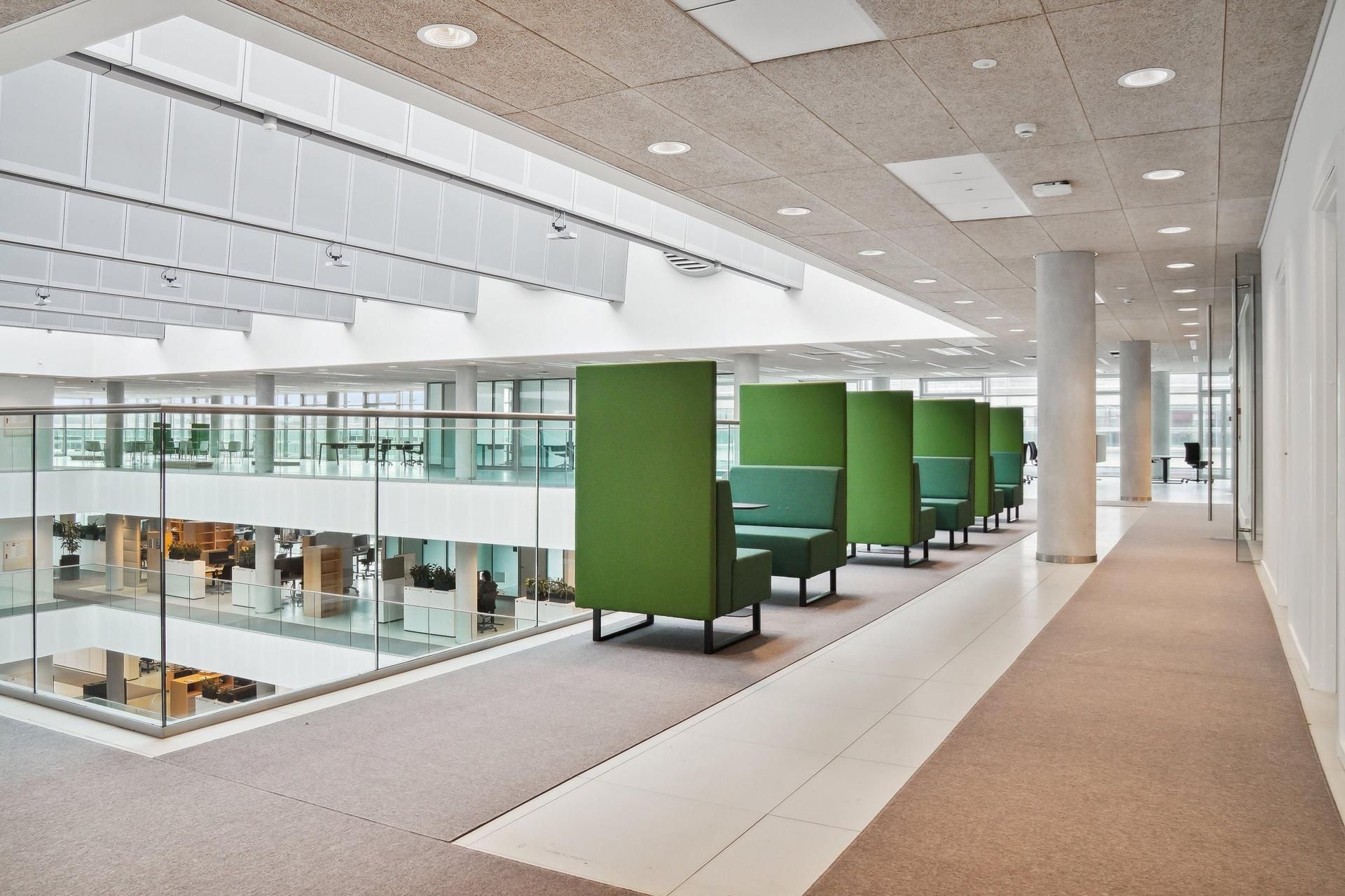 Grønne kontormøbler placeret i et stort, moderne kontor med glasvinduer og lyse lofter