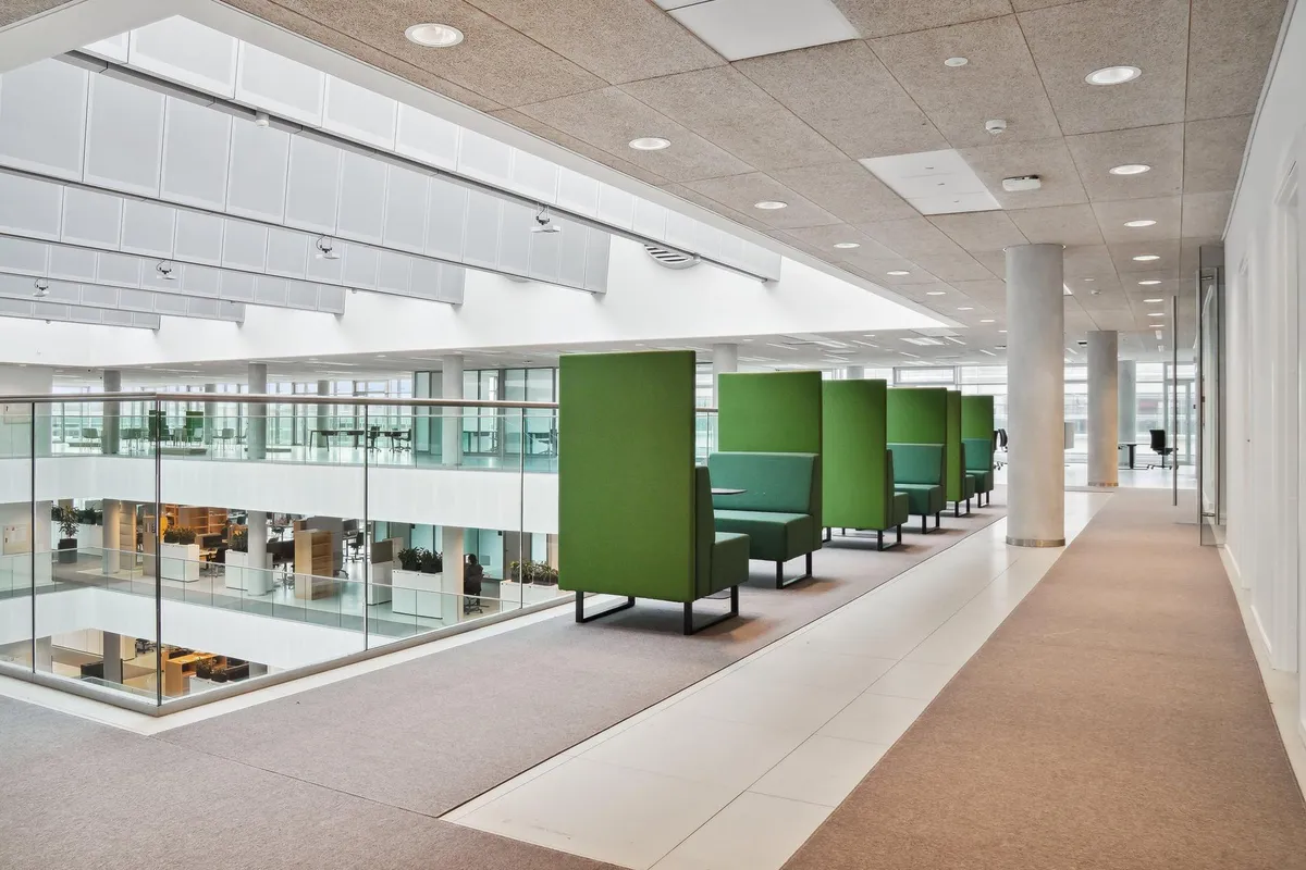 Grønne kontormøbler placeret i et stort, moderne kontor med glasvinduer og lyse lofter