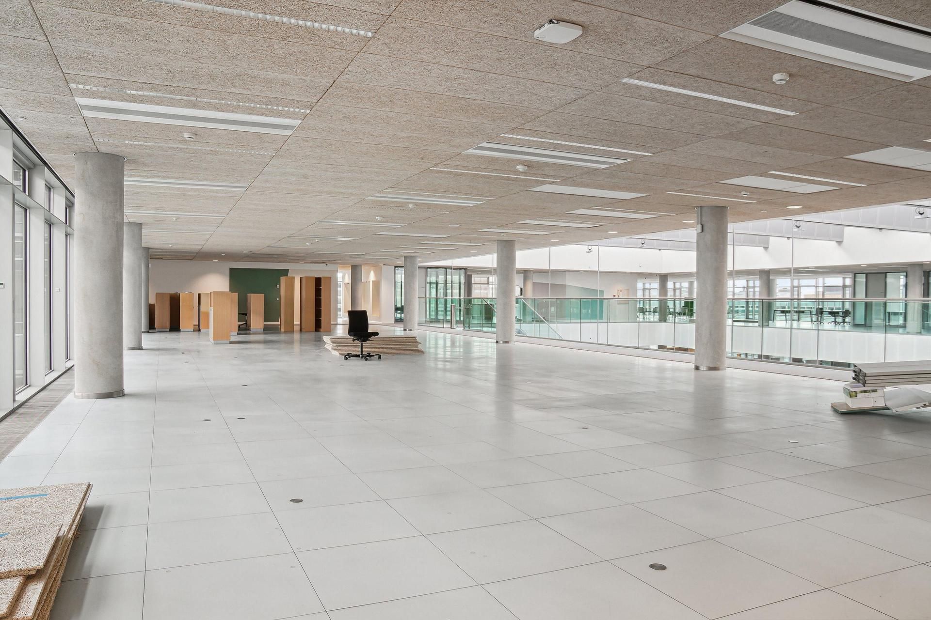 En stor, lys hall med hvide fliser og glasvinduer med udsigt over Amager Fælled, to søjler og flere lære i bunden af billedet