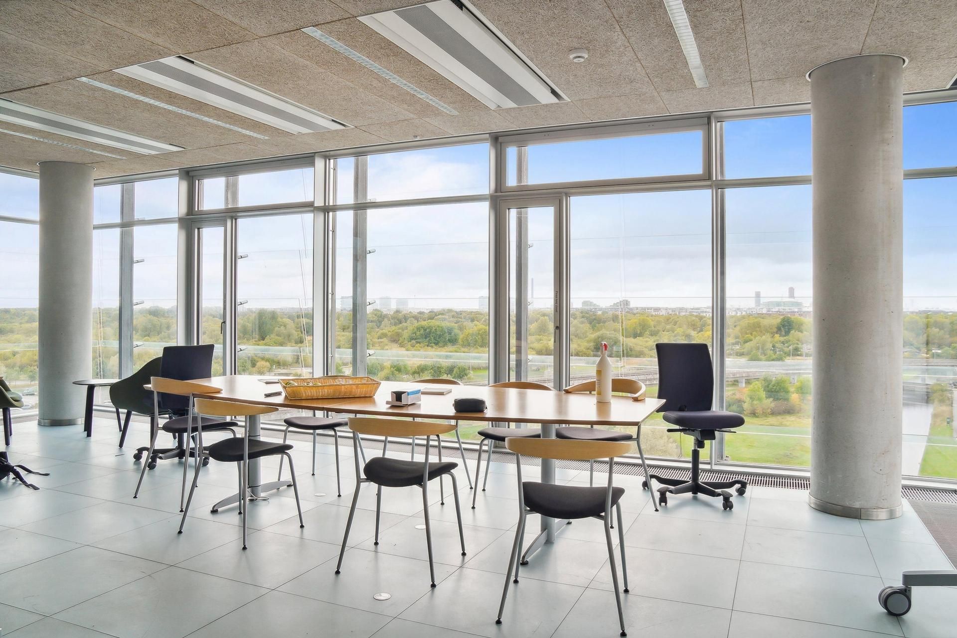 Kontorområde med store vinduer og udsigt over Amager Fælled, hvor man ser flere kontormøbler og udstyr