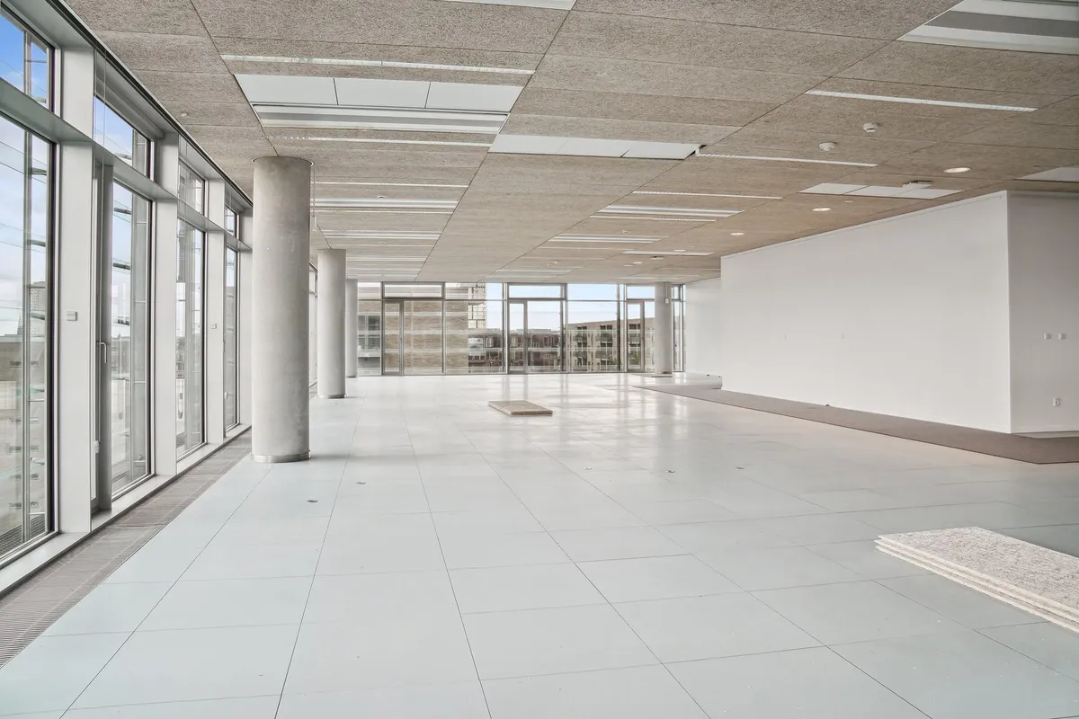 Store hvide lokaler med gulv, vinduer og højt til loftet med en stor hvid væg og to lyse loftspaneler