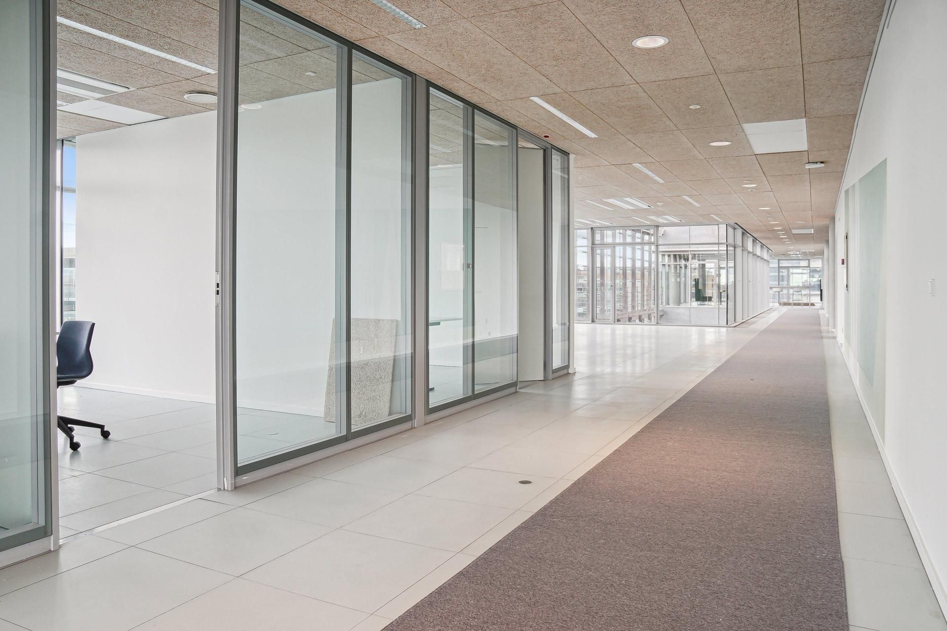 Glasvægge og hvide gulve i moderne kontor med en længdegang og møbler, der ser minimalistiske ud
