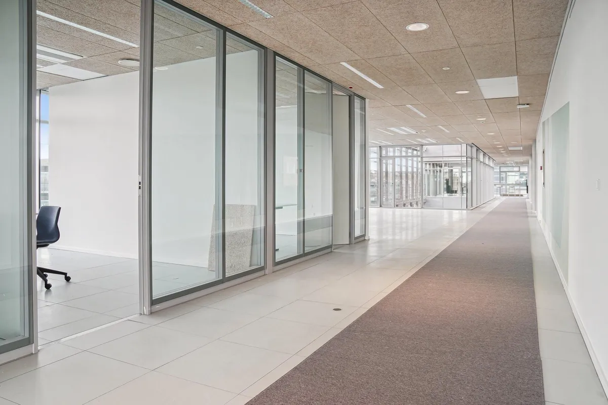 Glasvægge og hvide gulve i moderne kontor med en længdegang og møbler, der ser minimalistiske ud