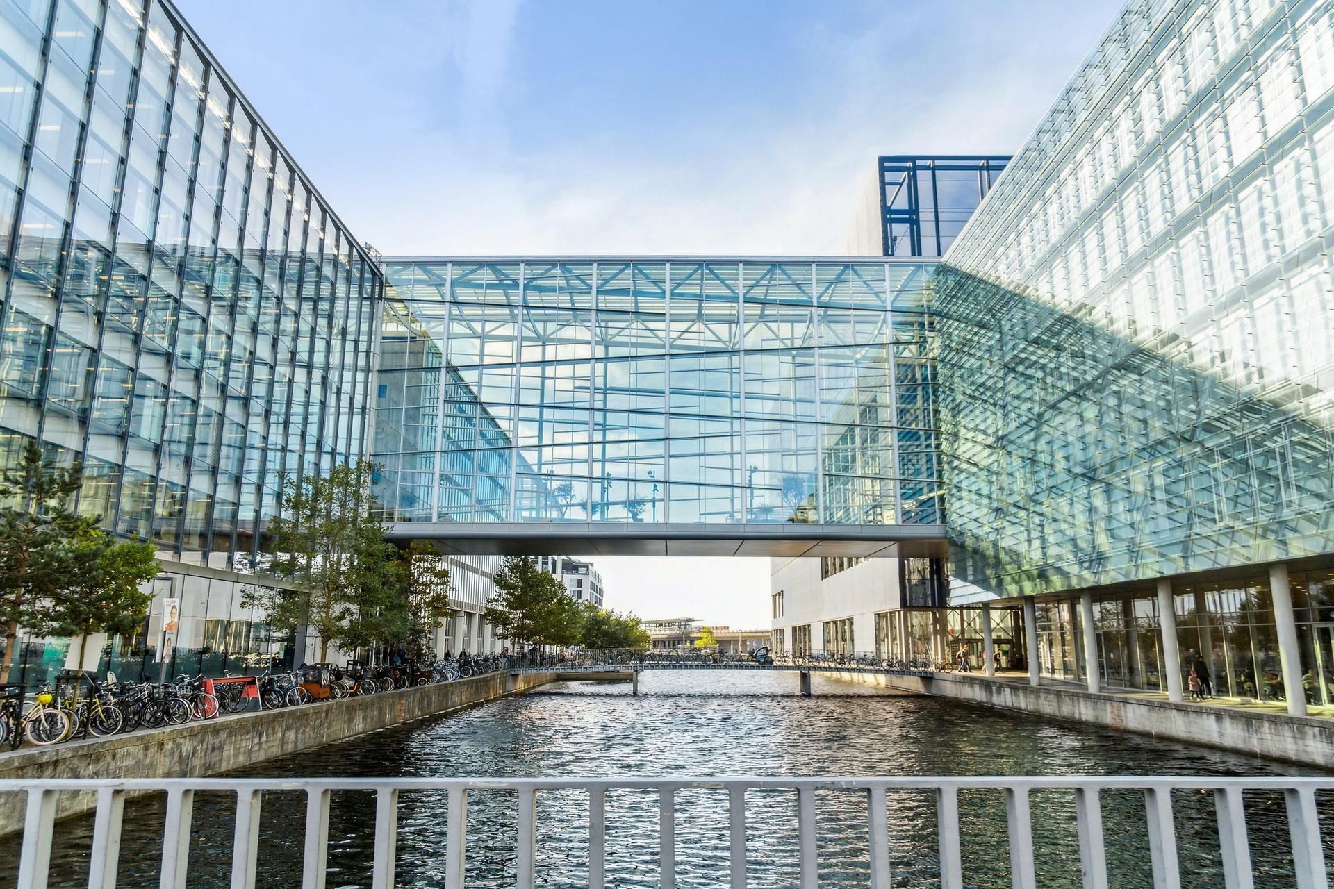 Bygninger med glas facader og gulv til lofts vinduer, der vender ud mod en lille vandvej med en bro, og mange cykler