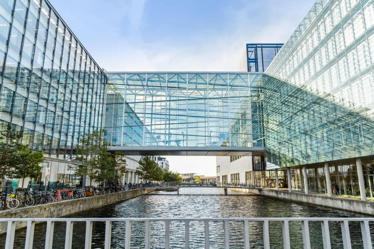Bygninger med glas facader og gulv til lofts vinduer, der vender ud mod en lille vandvej med en bro, og mange cykler