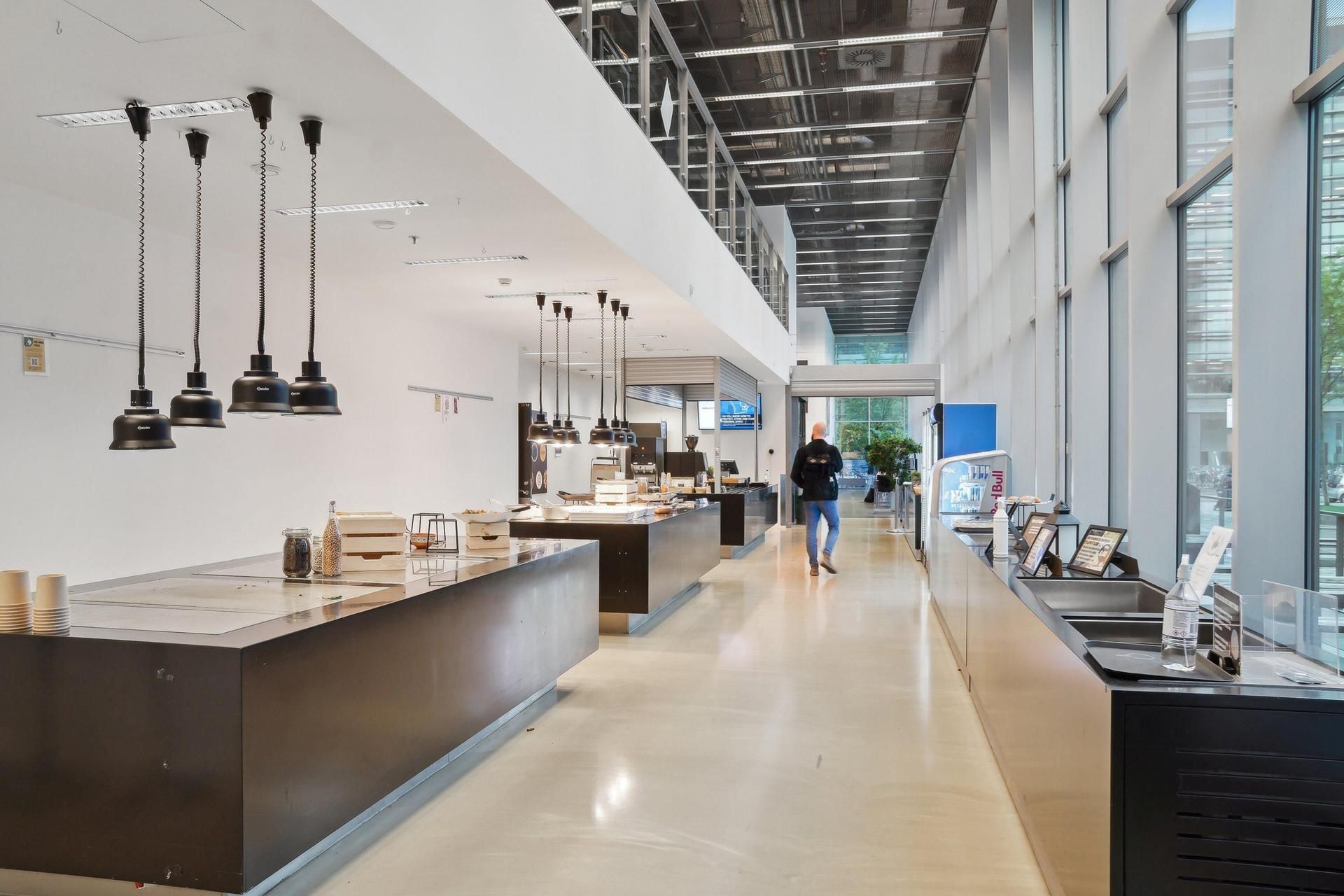 Mænd i kø for at købe mad i et moderne og veludstyret spisestue med store vinduer og moderne interiør