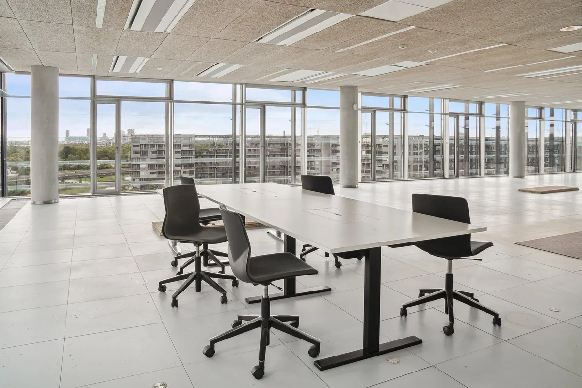 Moderne mødelokale med høje glasvinduer og udsigt over byen. Lang hvid bord med fire stole. Ingen mennesker i rummet.