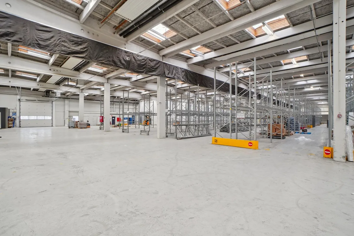 Et stort industrilager med metalliske opbevaringsstel og lyse lofter, fuld af paller og forskellige varer til fragt og lager.