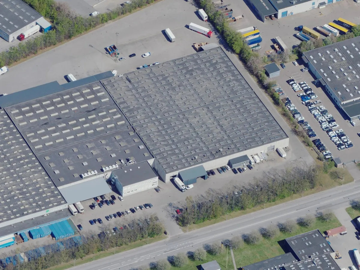 Lagerbygning med store parkeringspladser og masser af lastbiler i nærheden af en hovedvej og andre bygninger