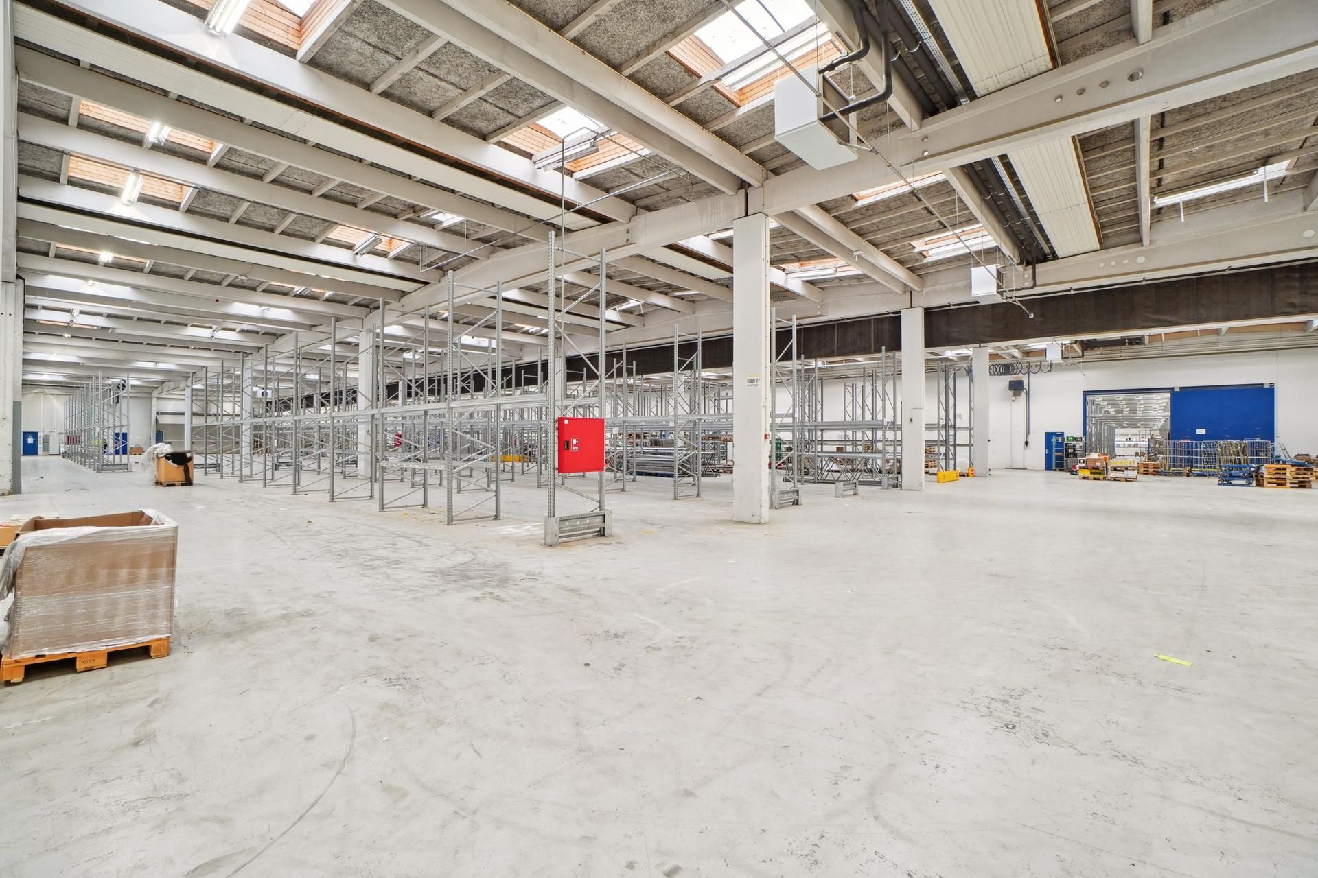 Industriel lagerhal med store lagerhylder og moderne opbevaringssystemer. Gulvet er renset, og der er masser af plads til
