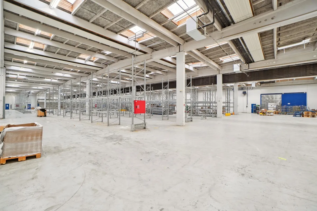 Industriel lagerhal med store lagerhylder og moderne opbevaringssystemer. Gulvet er renset, og der er masser af plads til