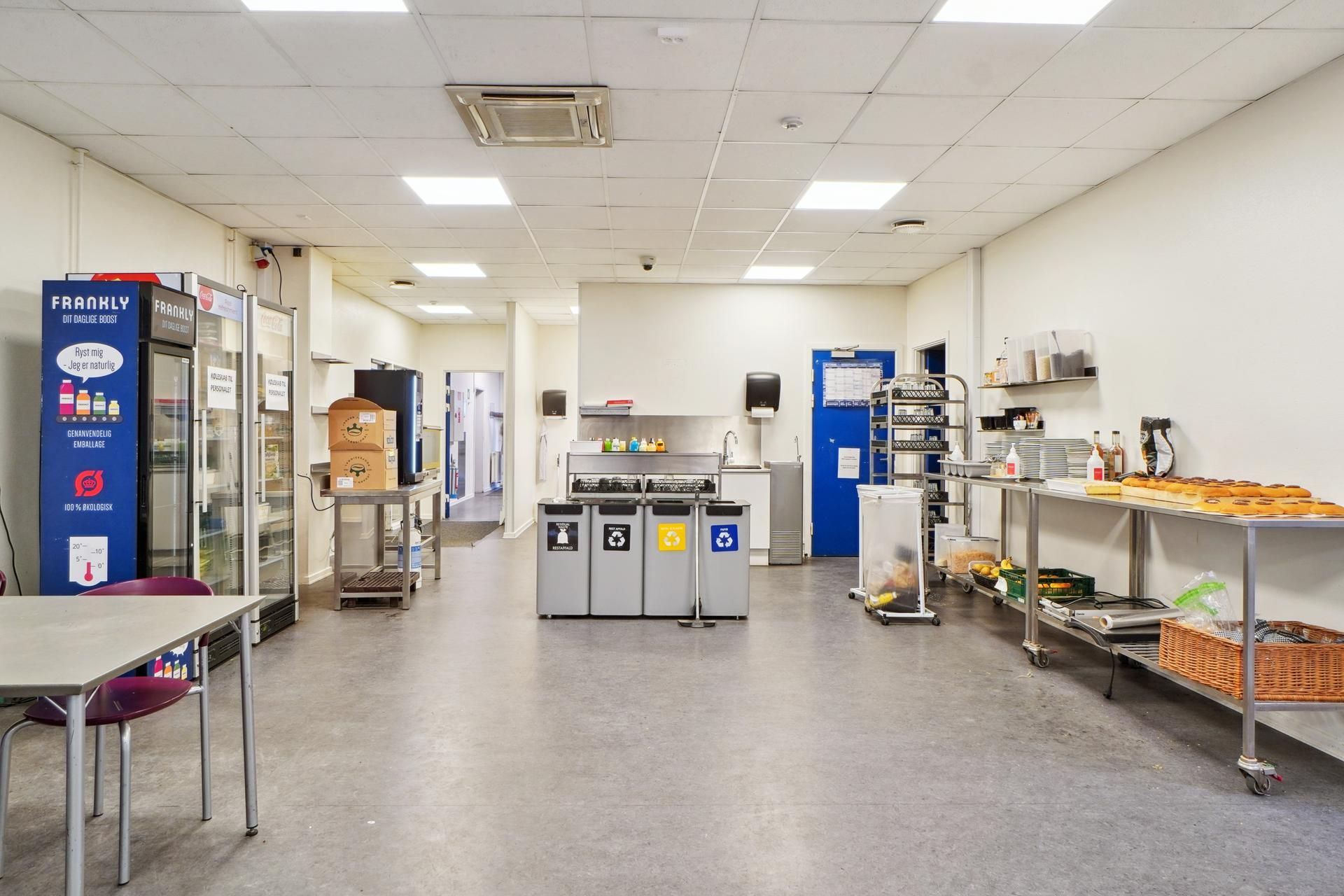 Køkken med to køleskabe, 3 opsamlingscontainere, stol, skraldspande, bord, og madkurve samt brødrister og bøfler