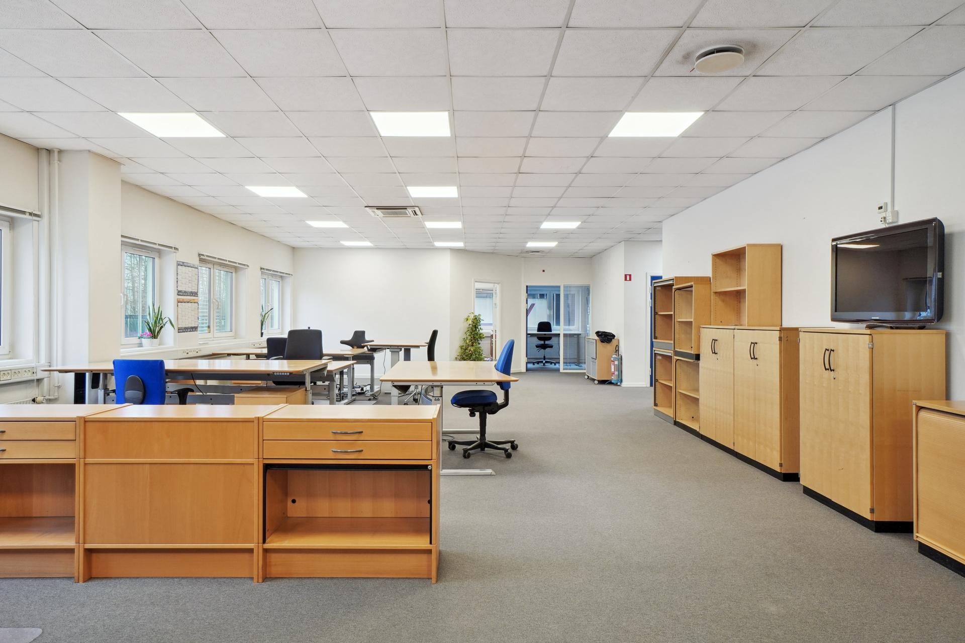 Et moderne, lyse og rummeligt kontor med lysegrå gulvbelægning og lyseblå vægge samt en række skriveborde og stole