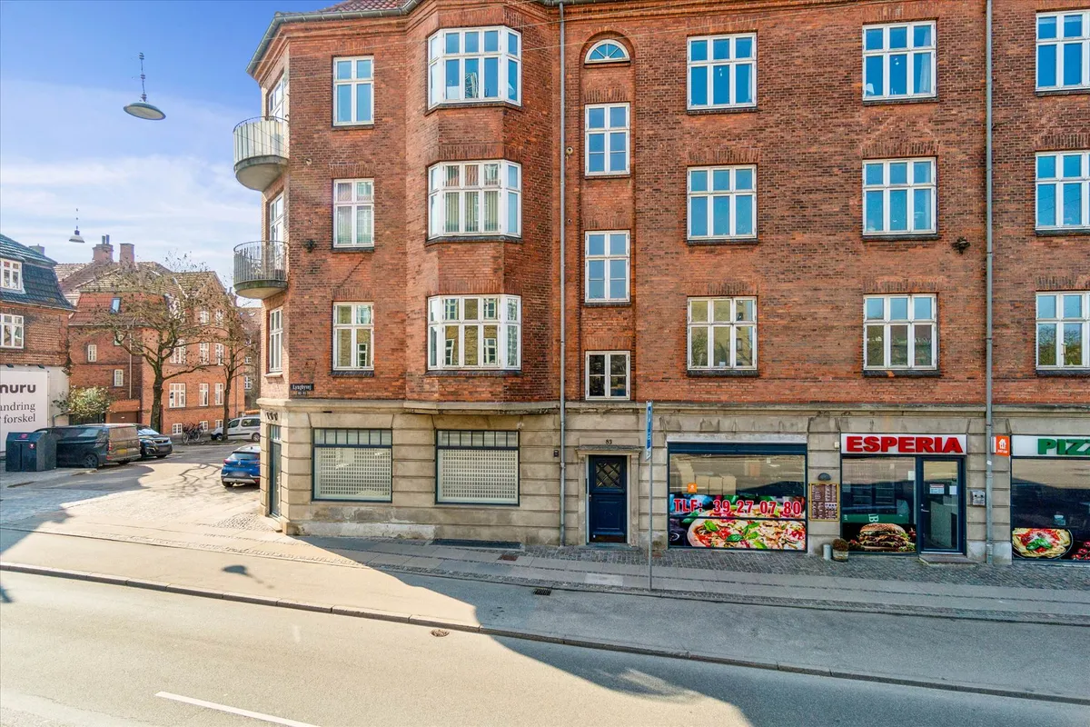 En to-etagers lejlighedsbygning med røde mursten og mange vinduer og balkoner, samt en restaurant og pizzeria med en pizza