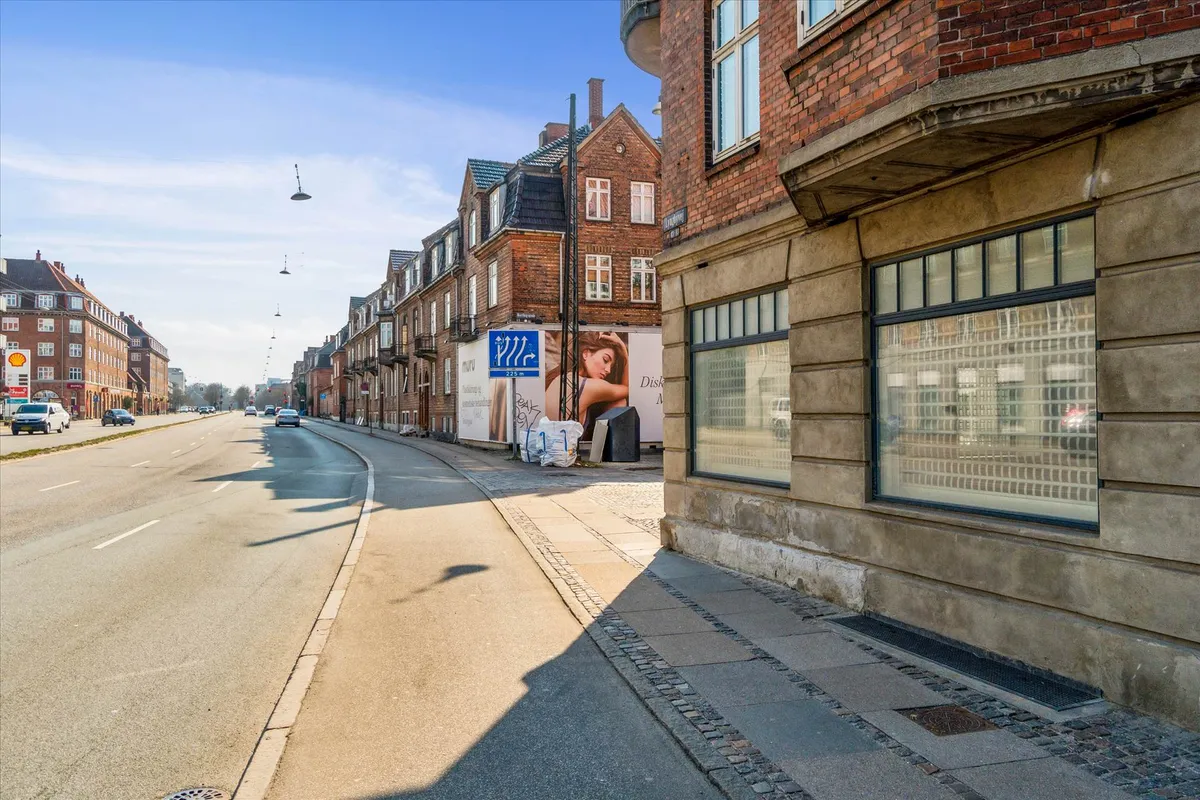 En bred hovedvej med biler og et lejlighedskompleks med mange vinduer og reklameskilte