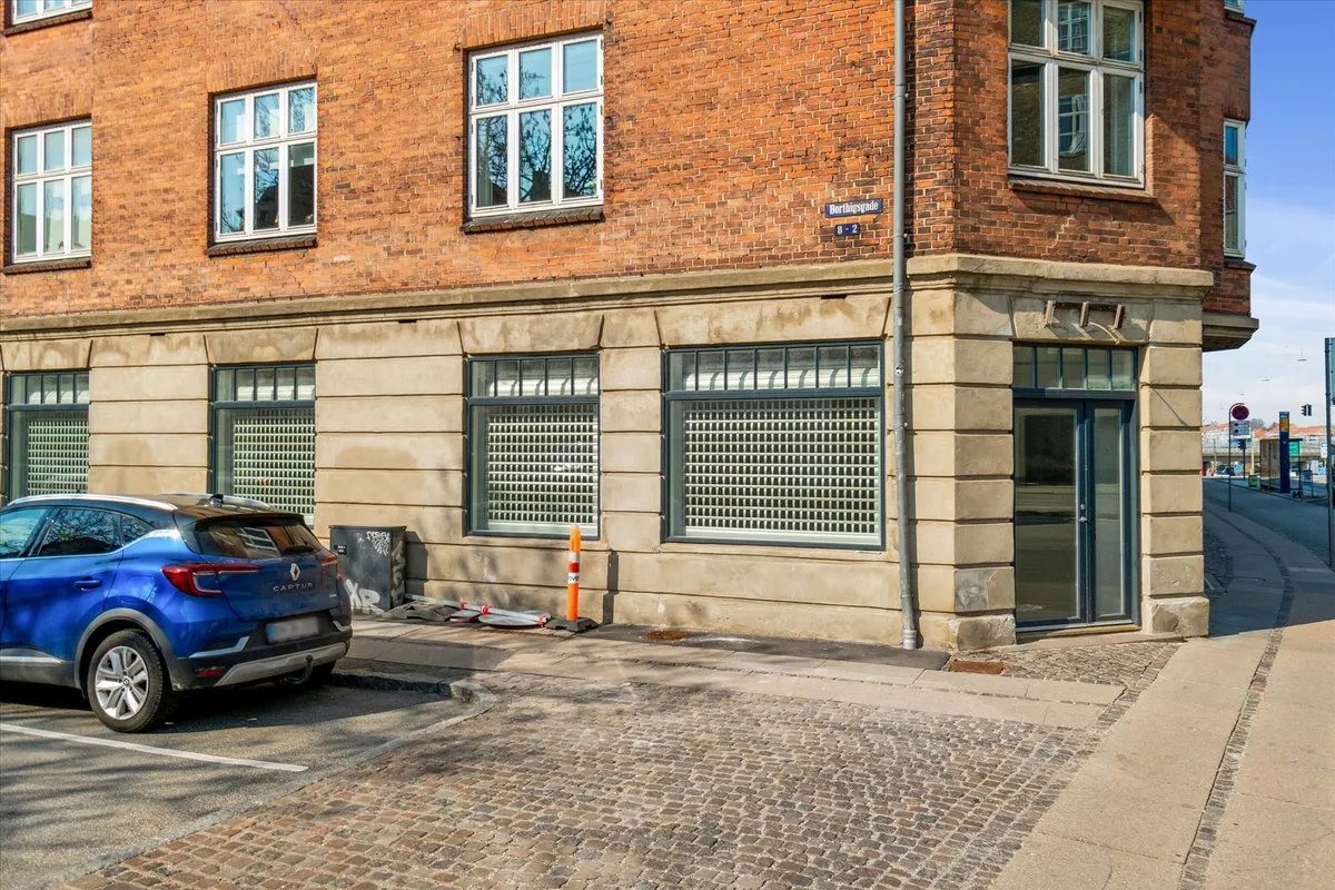 En blå Renault Captur parkeret ved siden af en bygning med røde mursten og vinduer, nummerplade og stående skjold over