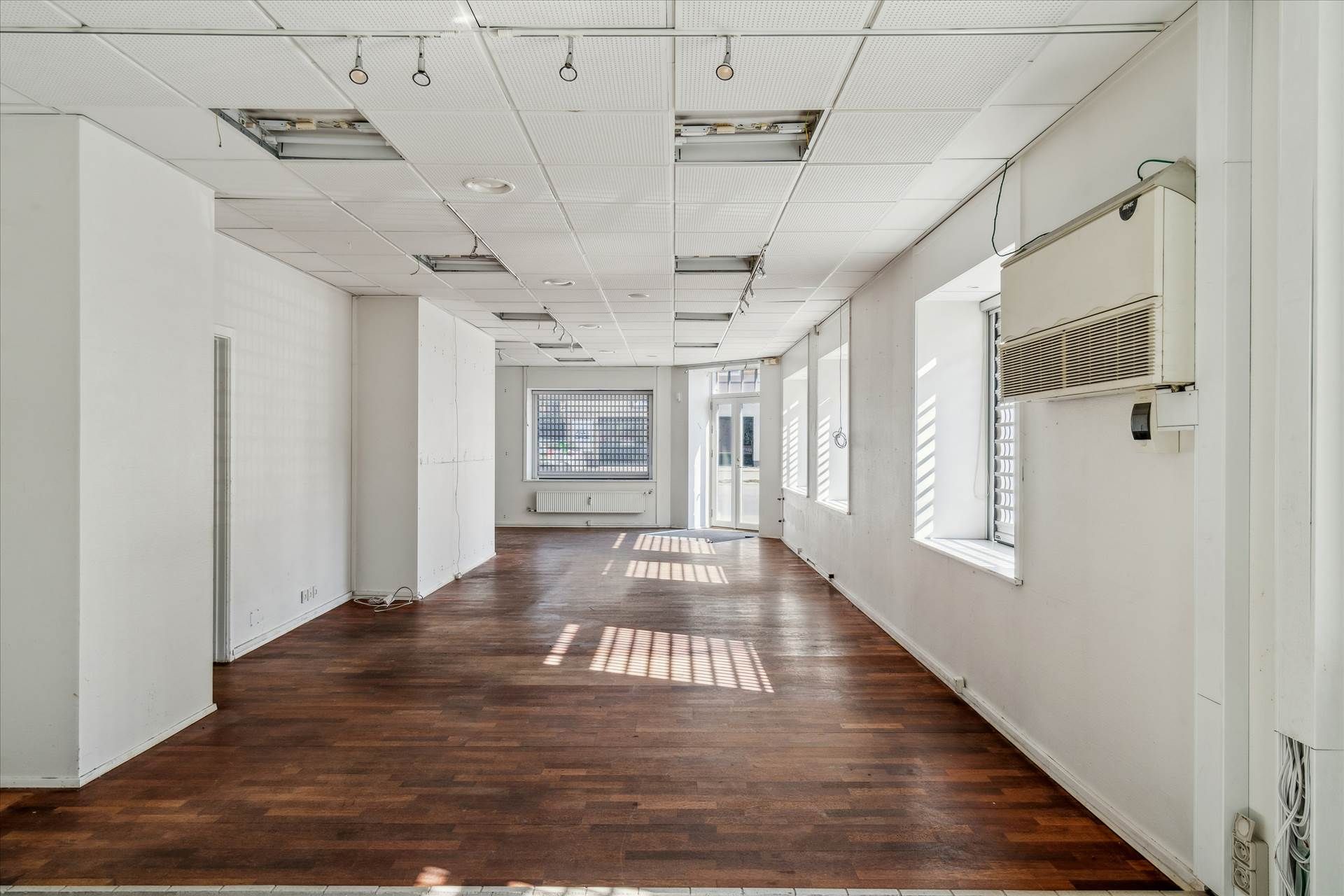 En tom kontorhjørne med hårdt trægulv og hvide vægge, hvor der er flere vinduer med glasruder og skråtage