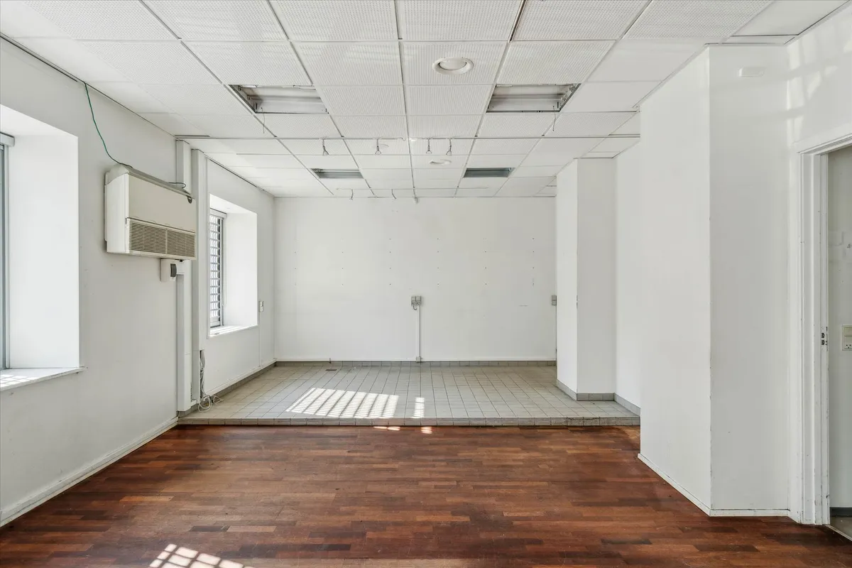 Et stort, tomt rum med hvide vægge og lofter samt trægulve og en klimaanlæg monteret på væggen
