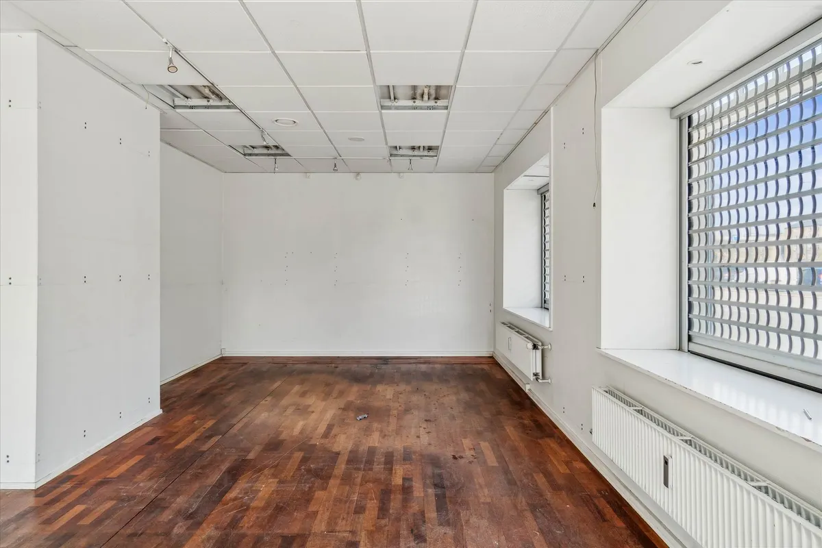 Et tomt lokale med hårdt gulv og hvide vægge og lofter med ventiler og en stor vinduesfront mod gaden
