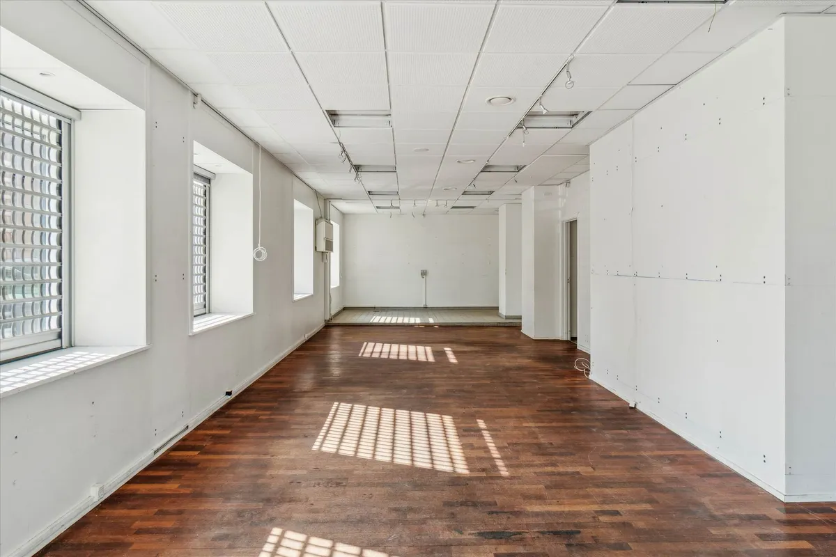 En stor og tom kontorejendom med hårdt trægulv, hvide vægge og vinduer med skyggekast indrammet af hvide ruder