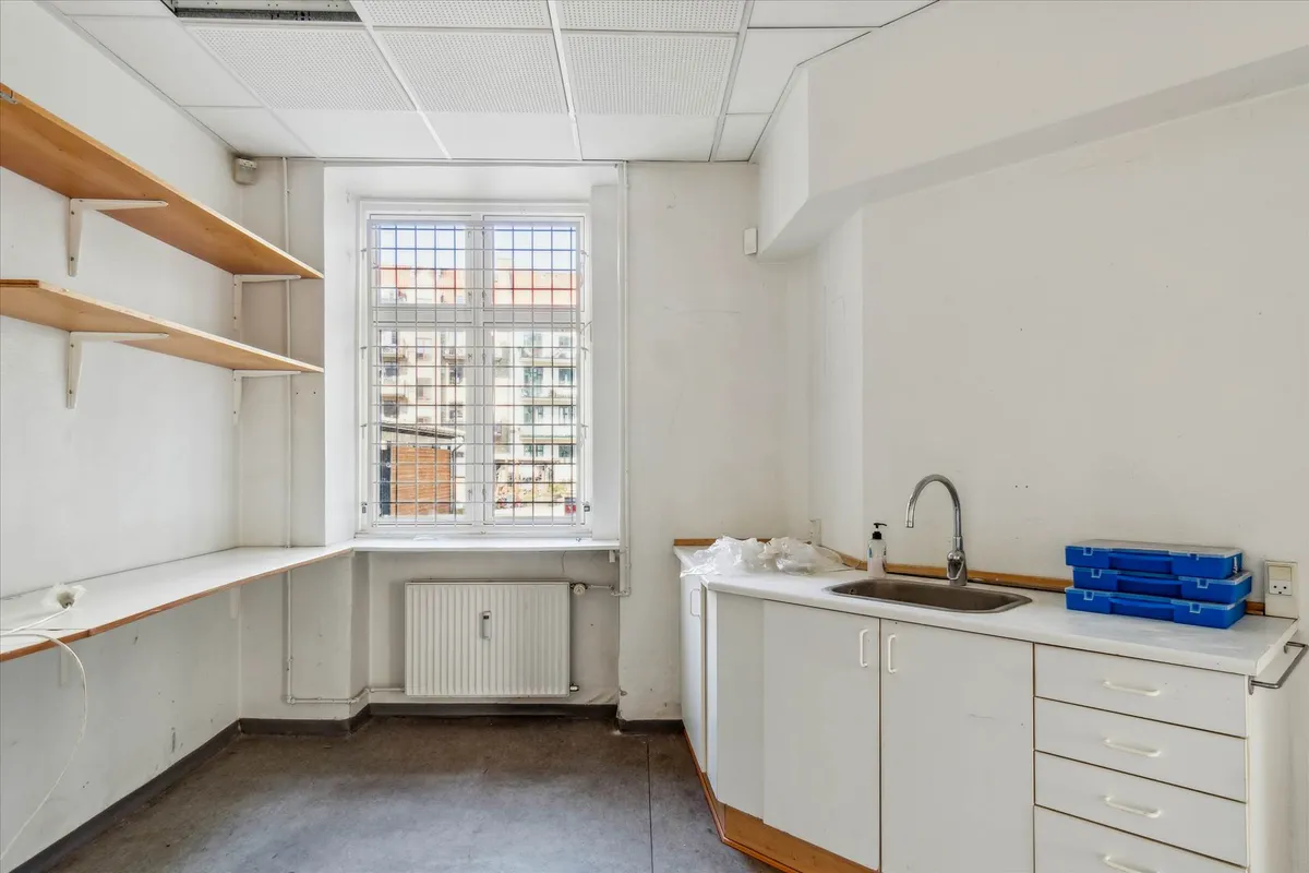 Hjørnebutik med køkken og udsigt til gaden samt to hylder og radiator under vinduet