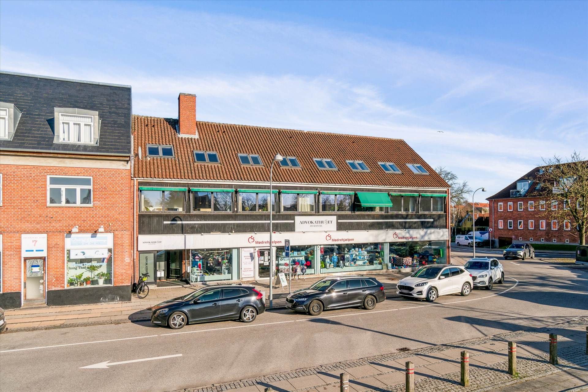 Gade med forretninger og biler parkeret på hjørnet, hvor en gågade og vejkryds mødes