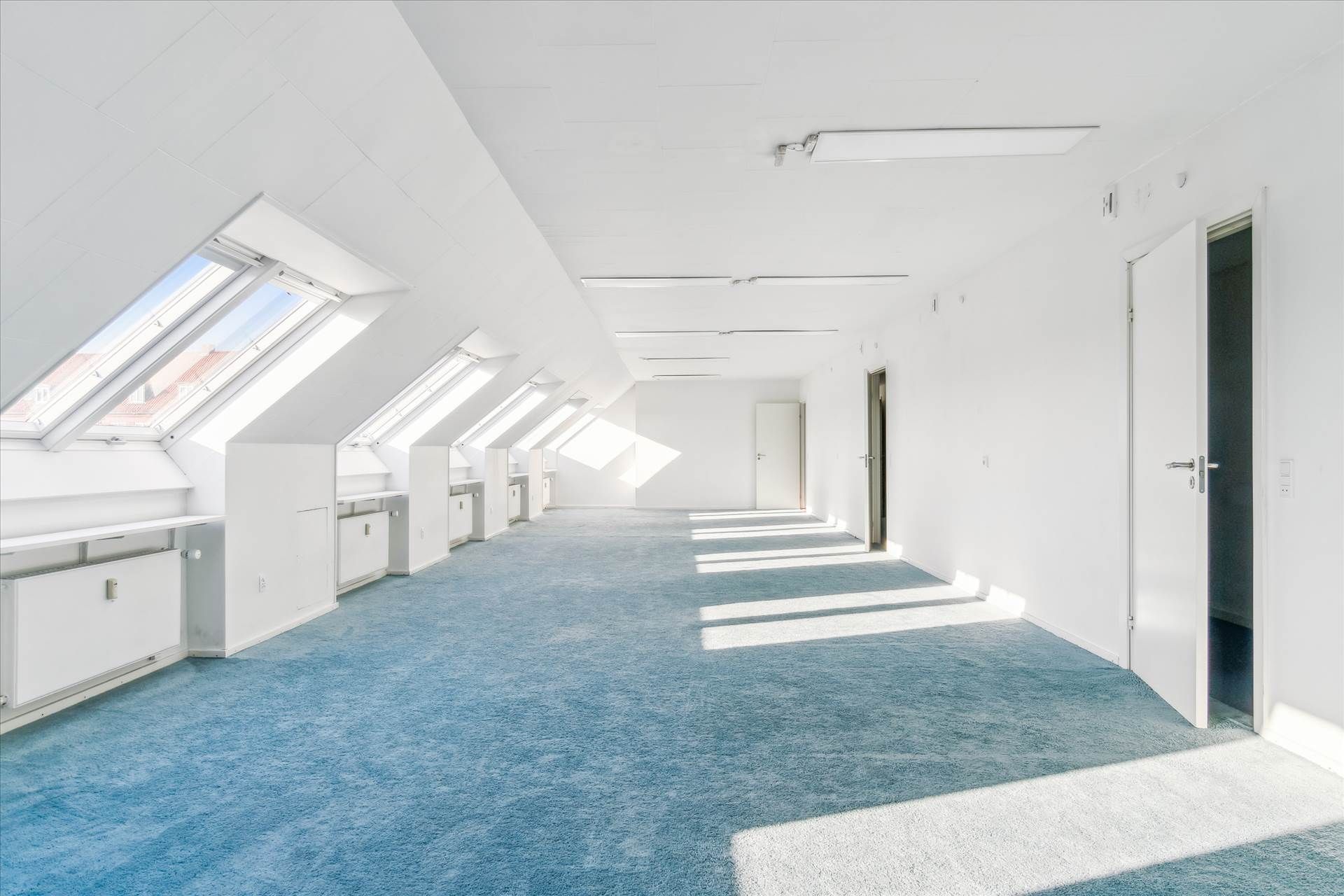 Lyst, stort kontor i hvidt og blåt, med store vinduer, hvide vægge og lyse lofter, samt lyse gulve