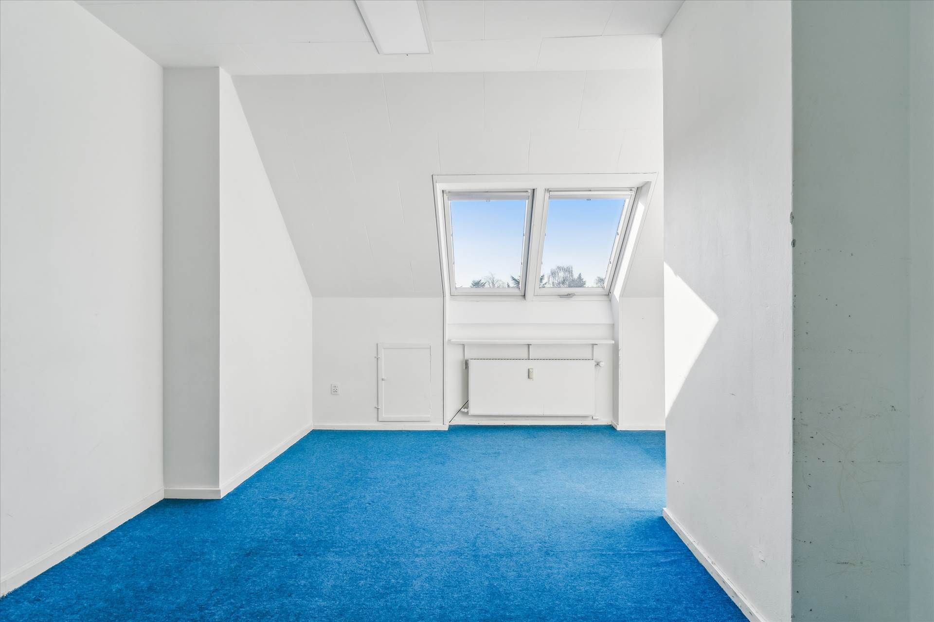 En tom stue med hvide vægge og blå gulv, samt et vindue med udsigt til en snefyldt skov med hvide vægge og et hvidt gulv.