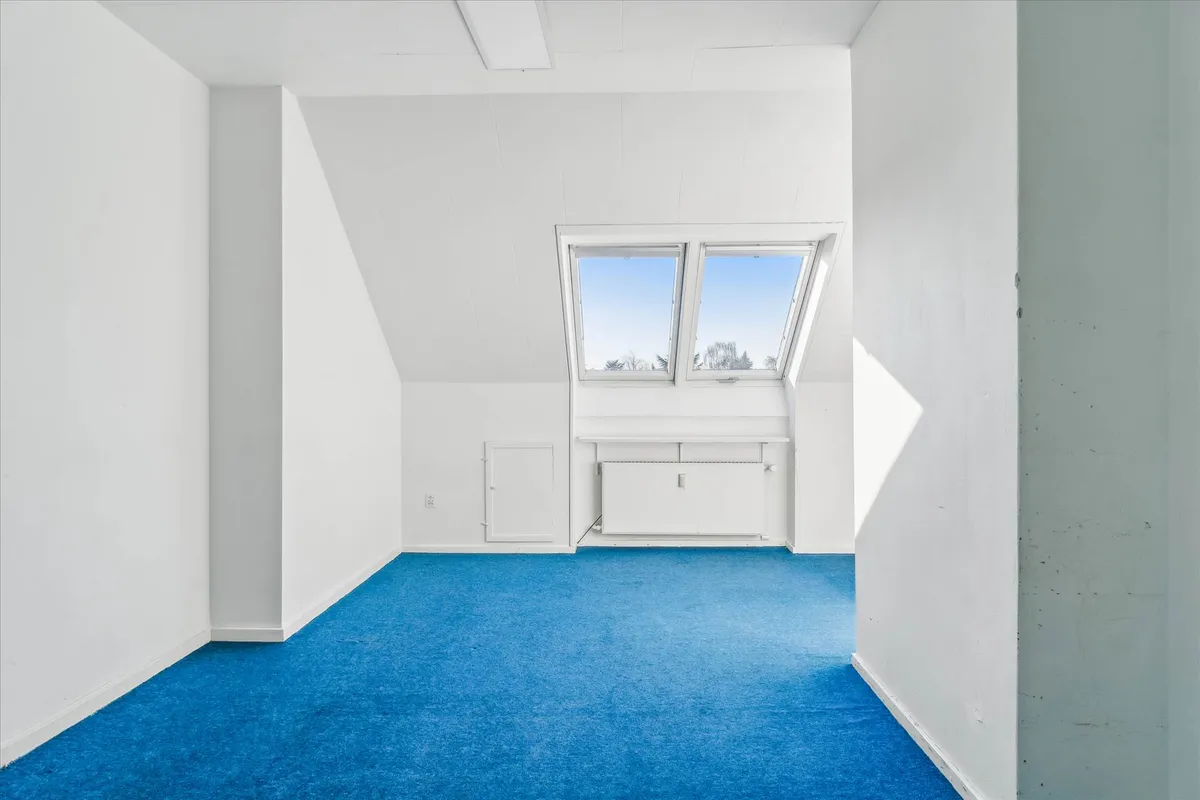 En tom stue med hvide vægge og blå gulv, samt et vindue med udsigt til en snefyldt skov med hvide vægge og et hvidt gulv.