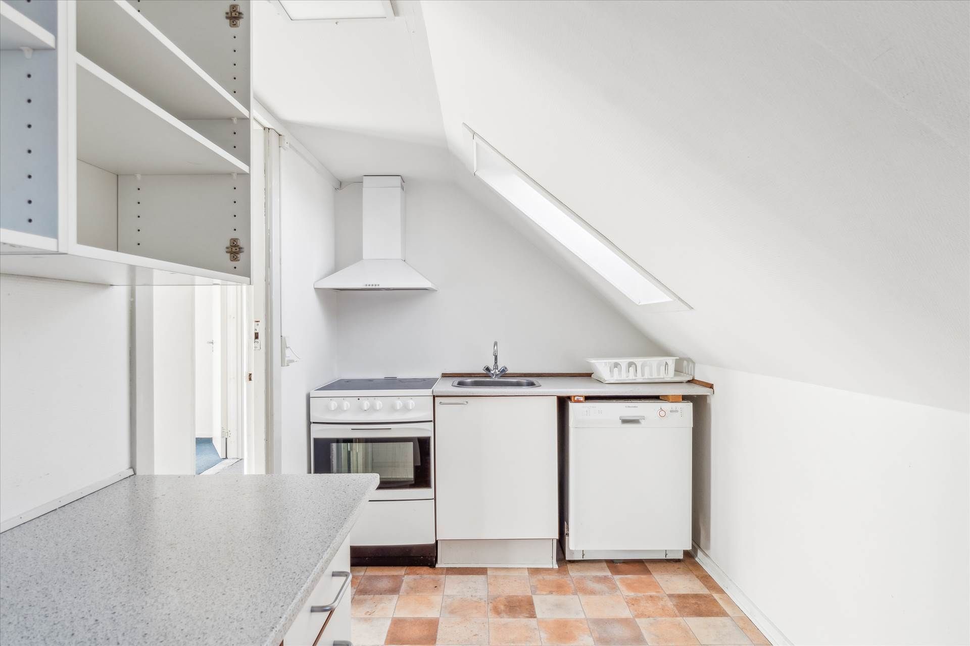 Værelse med køkken og loftsvindue, hvide vægge og møbler samt lysegule loftslofter og en lille køkkenhylde med en skuffe