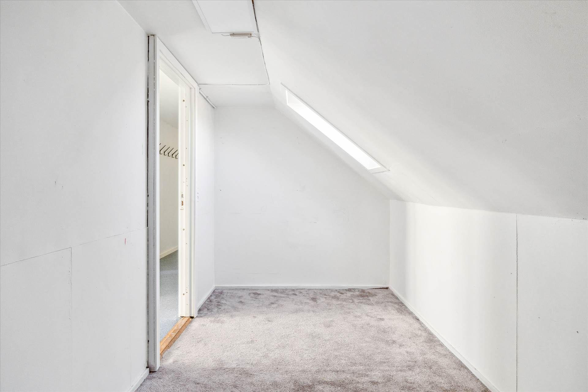 En tom, hvid vægget stue med en åben dør og gulvtæppe, hvor der er en lysstribe på loftet