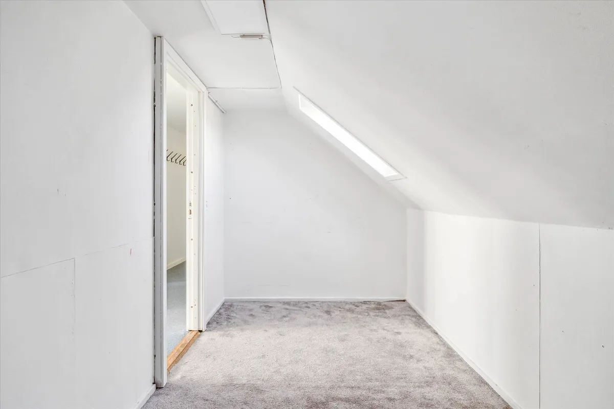 En tom, hvid vægget stue med en åben dør og gulvtæppe, hvor der er en lysstribe på loftet