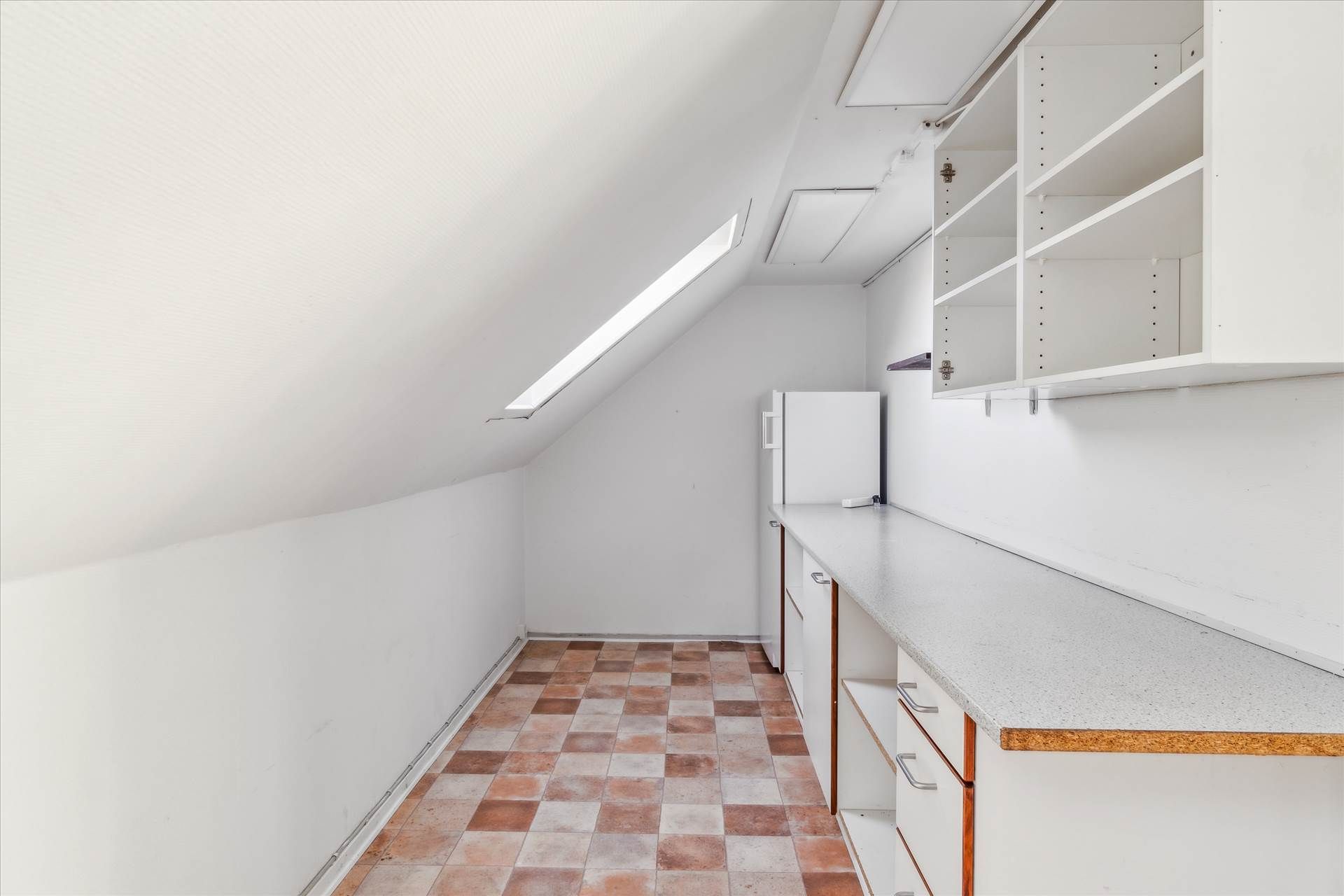 Hjørne loftsværelse med køkkendel, hvidt loft og vægge, loftsvindue og hvidt køleskab med møbler og bordplade