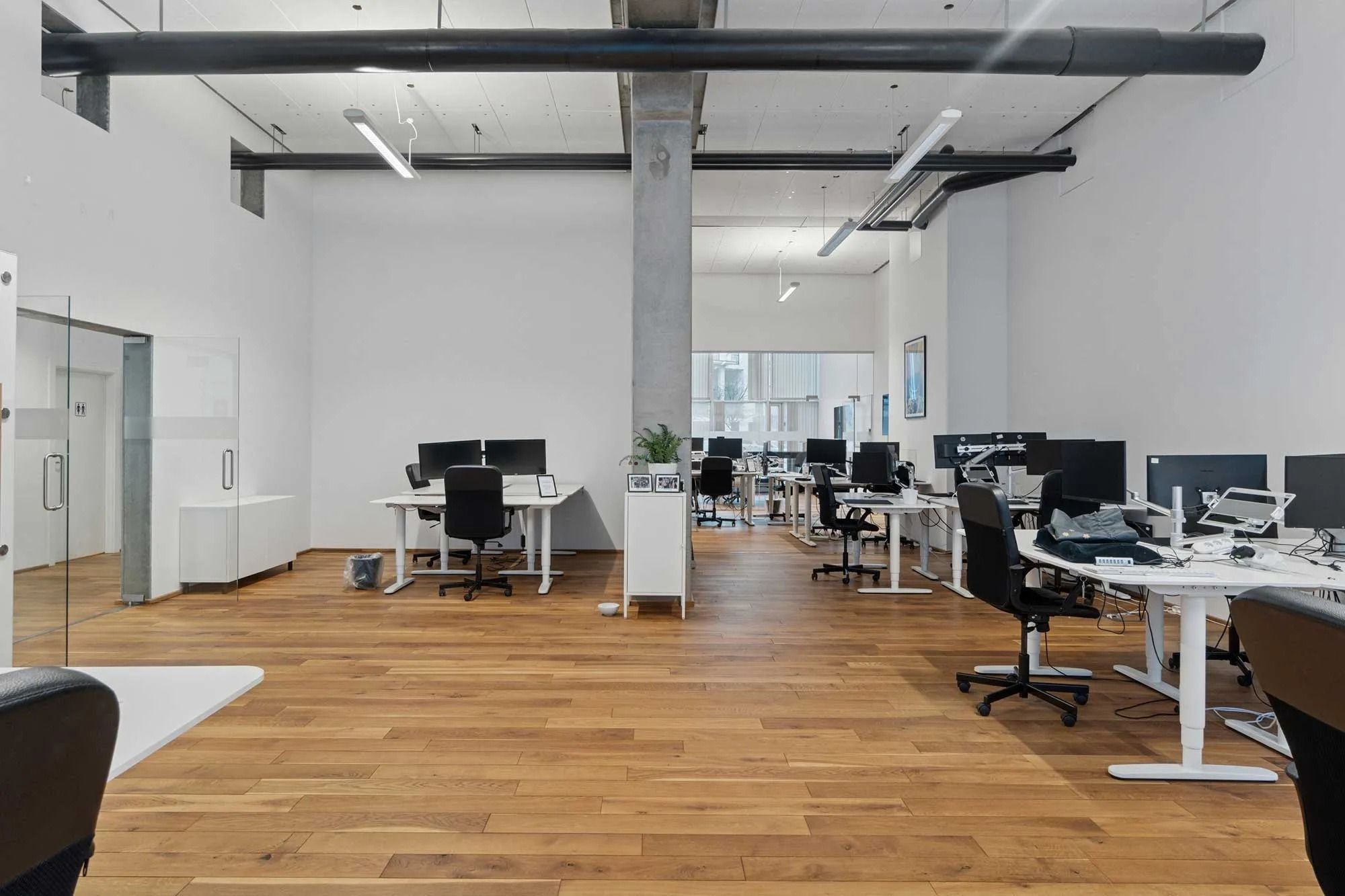 Moderne kontor med højloft og lyse loftslampe, hvide vægge, trægulve og ergonomiske kontormøbler