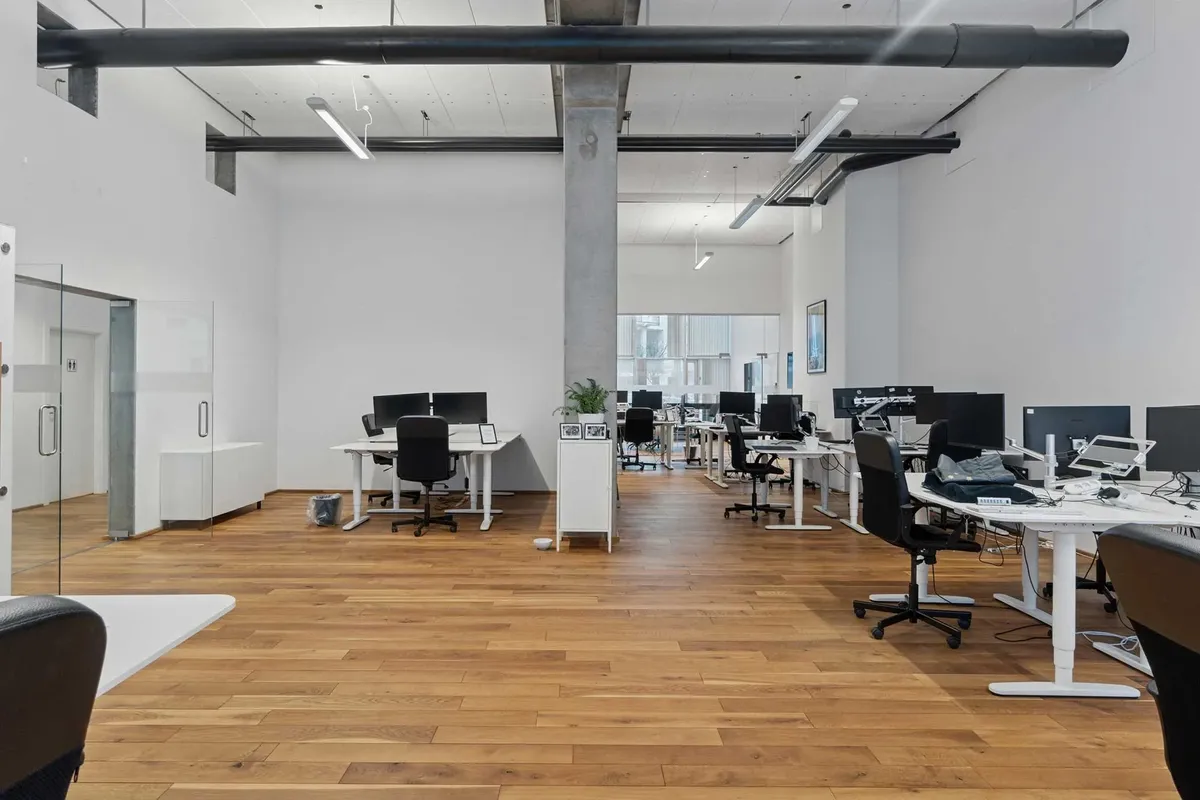 Moderne kontor med højloft og lyse loftslampe, hvide vægge, trægulve og ergonomiske kontormøbler