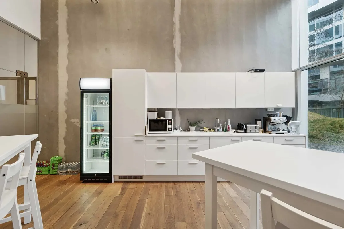 Moderne køkken med hvide møbler og lyse gulvplanker samt en stående køleskab med drikkevarer og en kaffemaskine på hylden